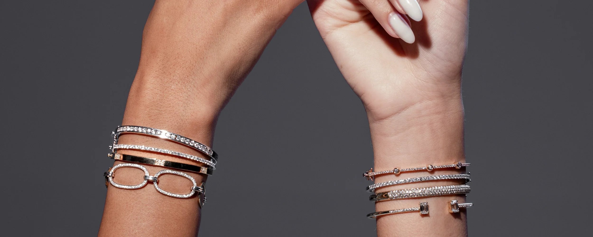 Close-up of a hand wearing multiple bracelets with diamonds on a dark background