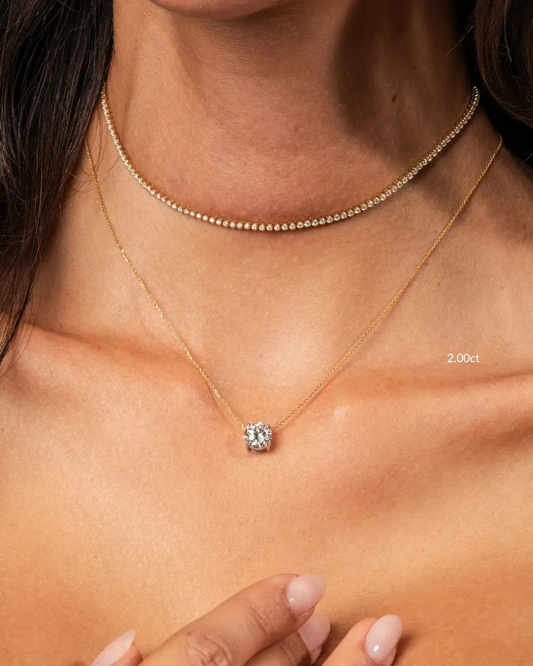 Elegant floating diamond necklace showcasing a round brilliant cut diamond on a gold chain, paired with a sparkling tennis necklace.