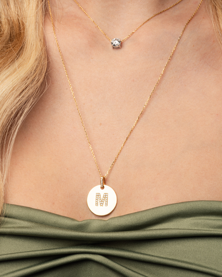 Close-up of a Love Letter Disk necklace with an 'M' pendant in 18ct gold, showcasing its certified diamond charm.