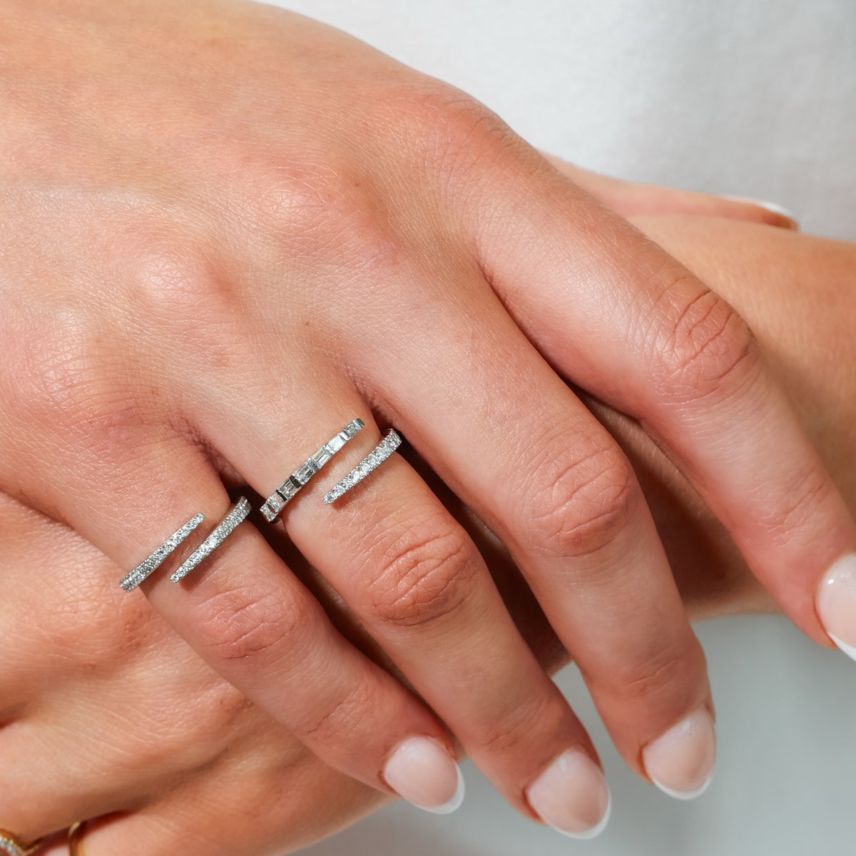 A close-up of a person's hand wearing diamond wrap rings, against a soft light gray background.