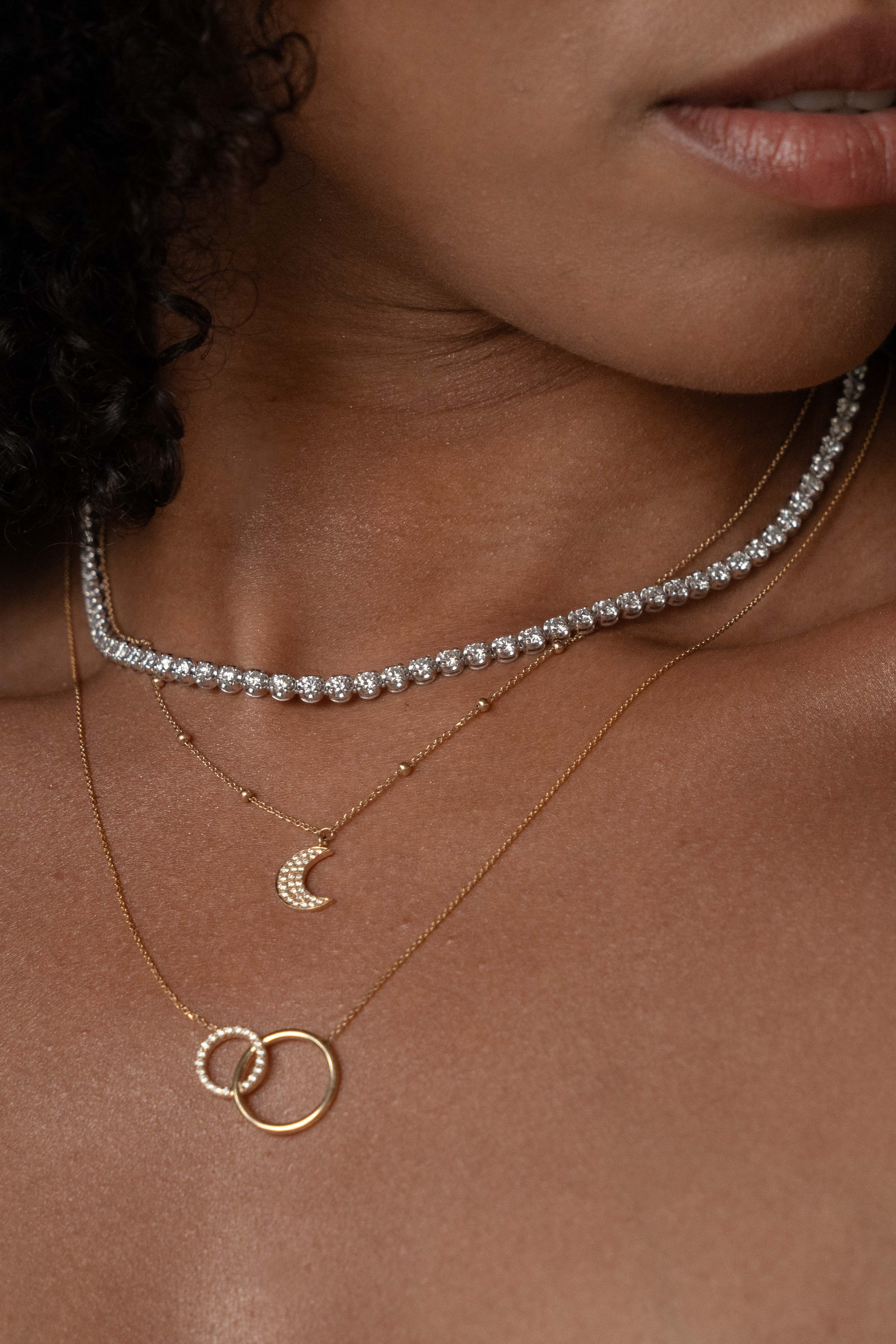 Close-up of a woman wearing a diamond necklace and a gold half moon necklace.