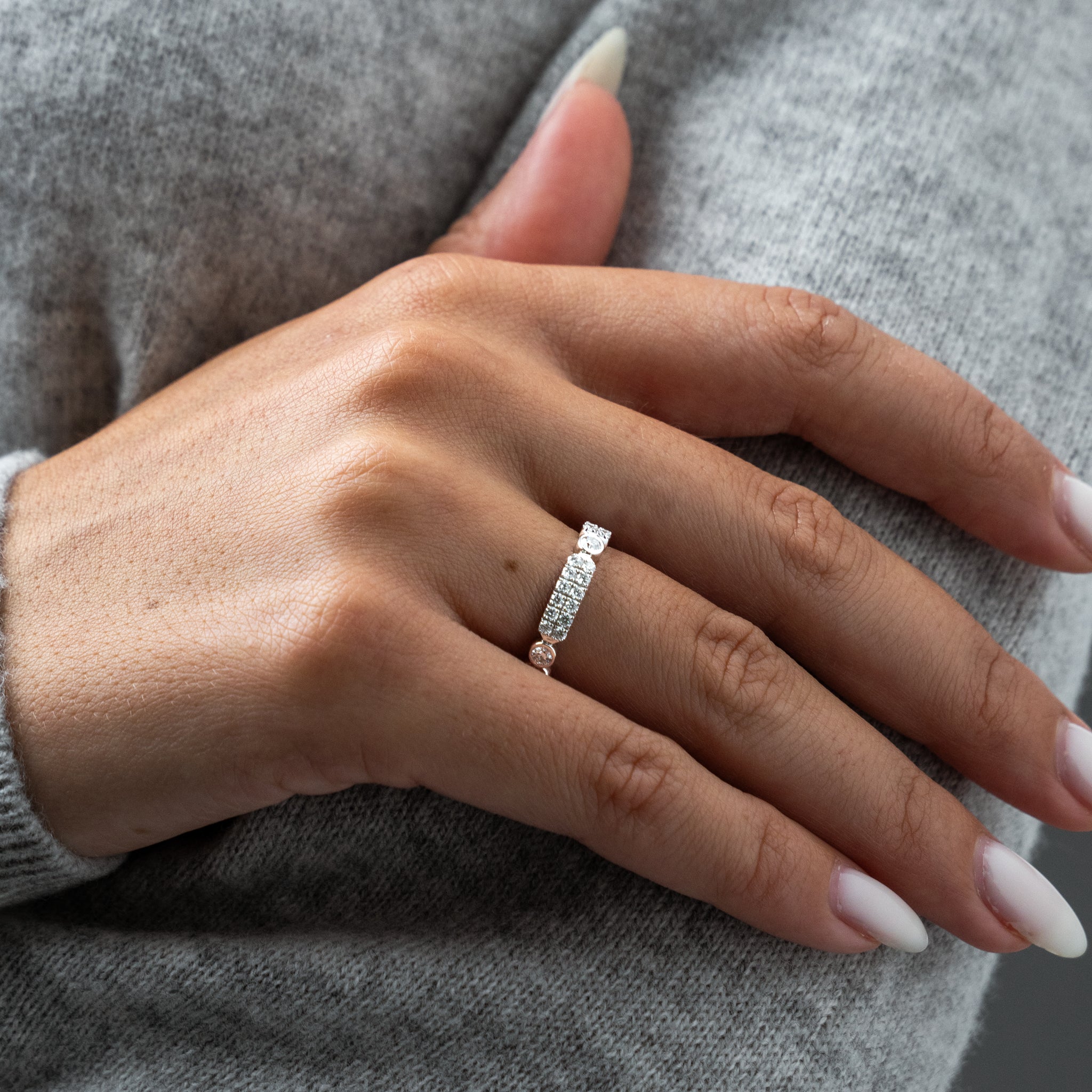 Hand wearing a diamond ring against a grey sweater background