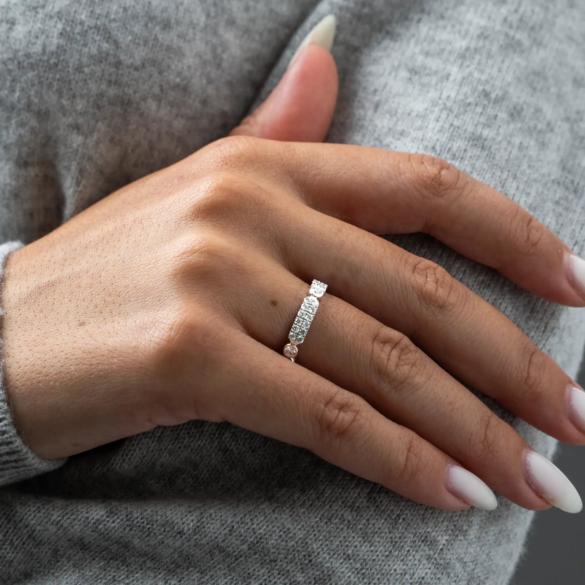 Hand wearing a diamond ring against a grey sweater background