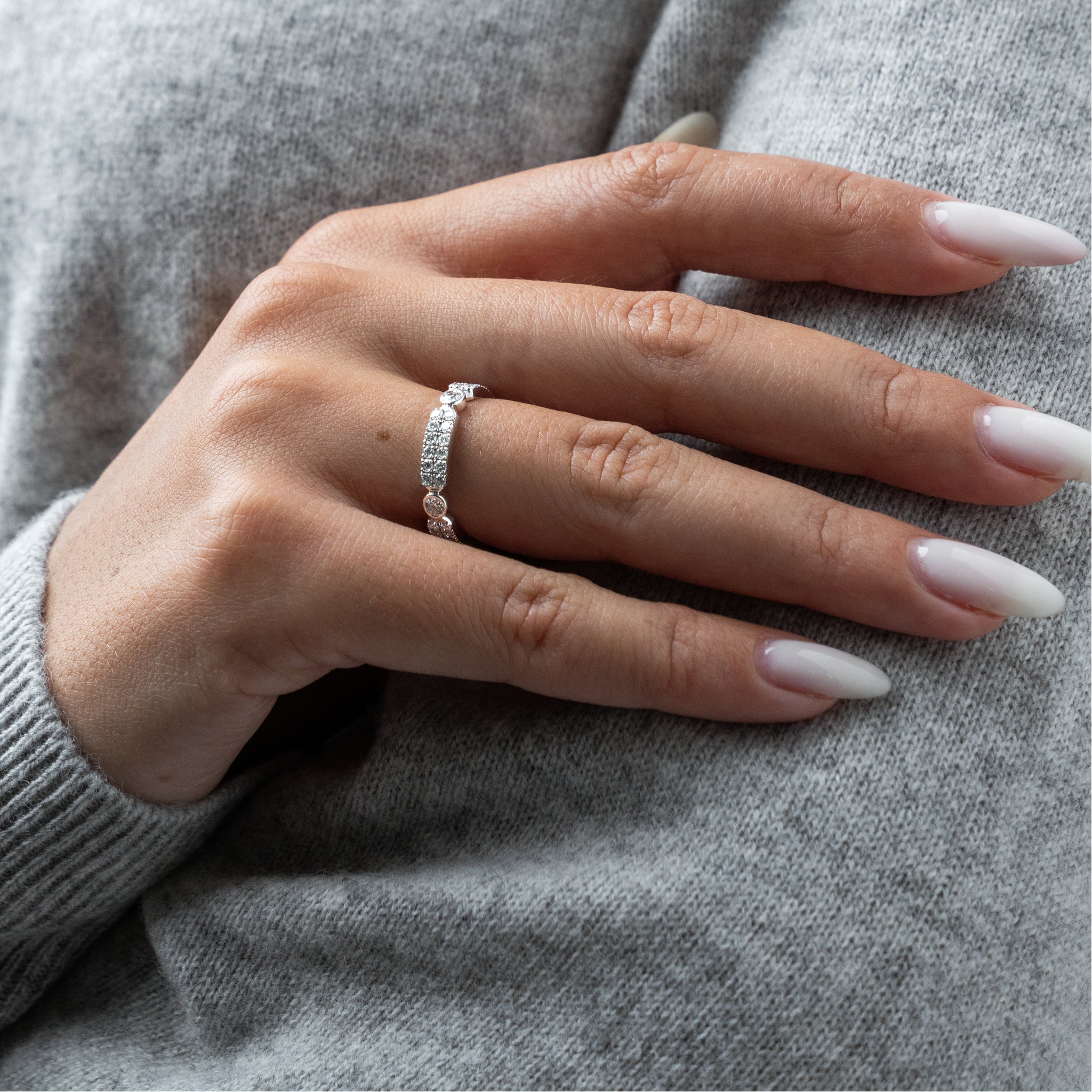 Close-up of a hand wearing a diamond ring on a gray sweater background