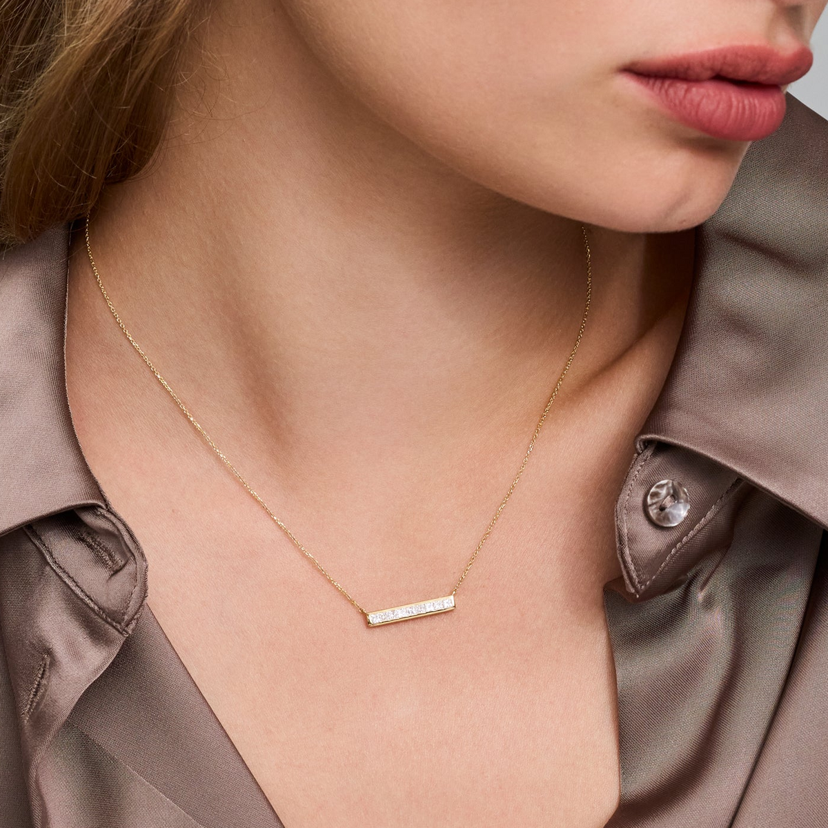 Model wearing a diamond bar necklace featuring a gold chain and princess-cut diamonds against a stylish satin shirt.