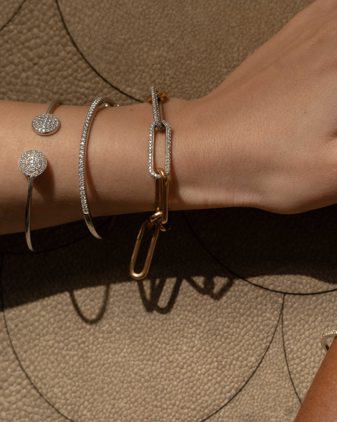 Close-up of a hand wearing diamond tennis bangles set in gold with a chunky chain link bracelet showcasing diamonds.