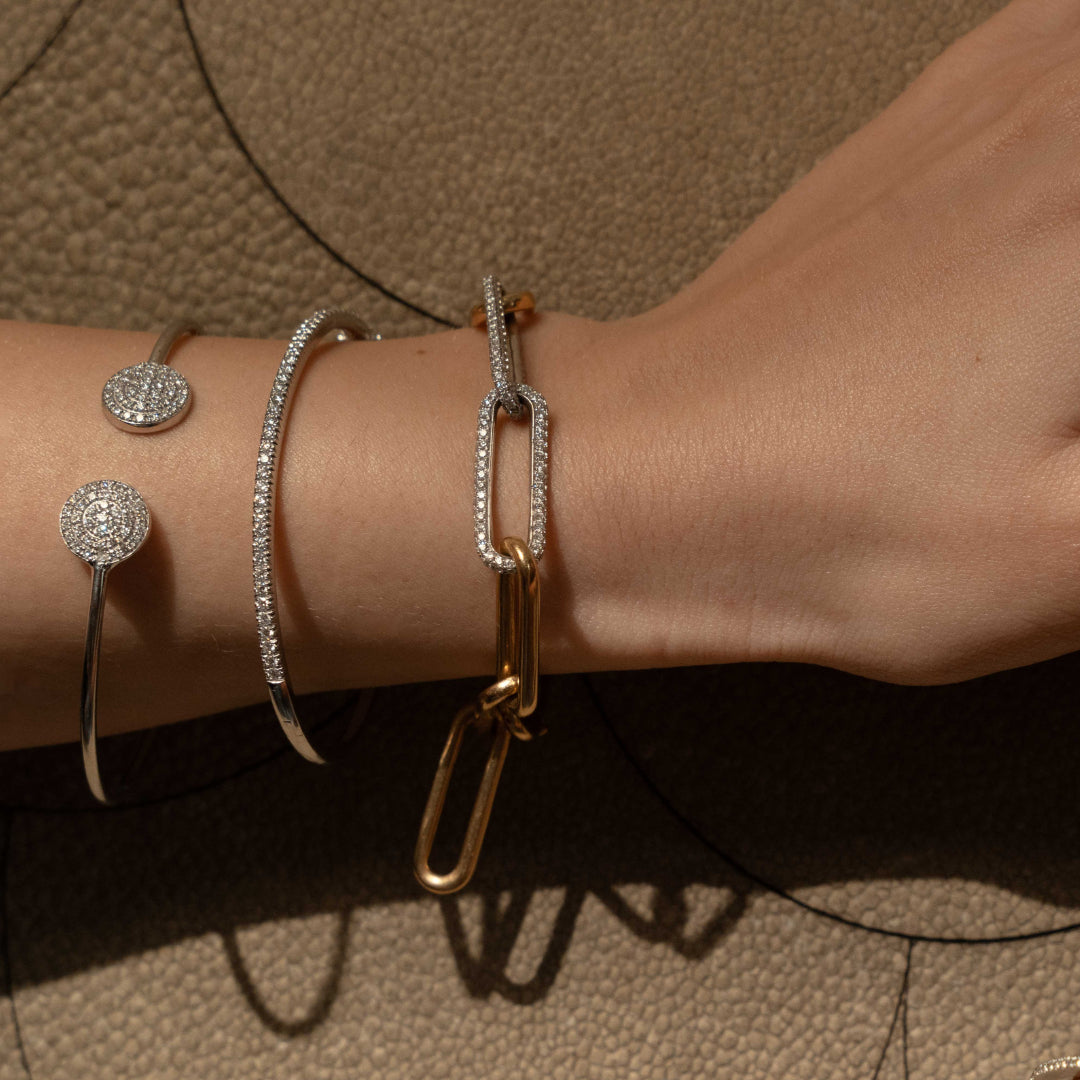 Close-up of a hand wearing diamond tennis bangles set in gold with a chunky chain link bracelet showcasing diamonds.