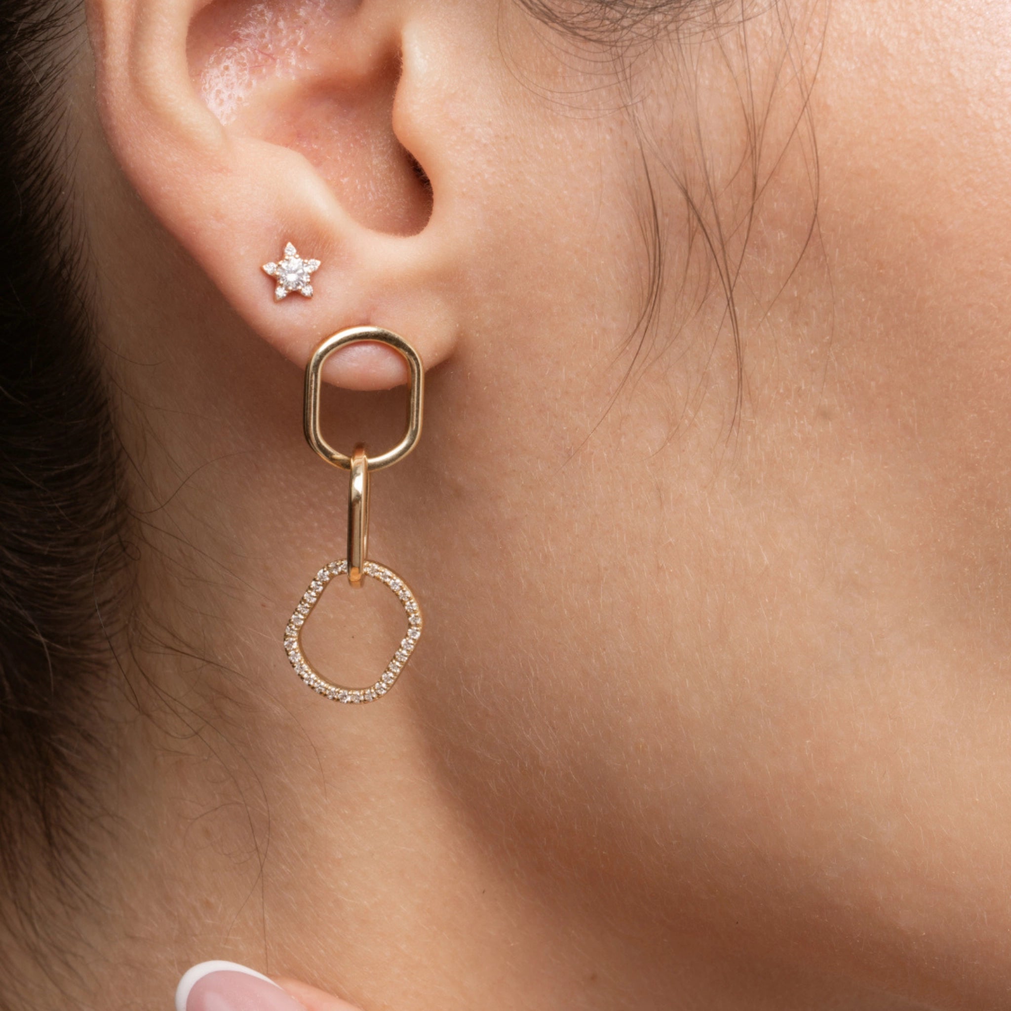 Close up of a woman's ear showcasing chain link diamond earrings and a solid gold star earring, highlighting style and elegance.
