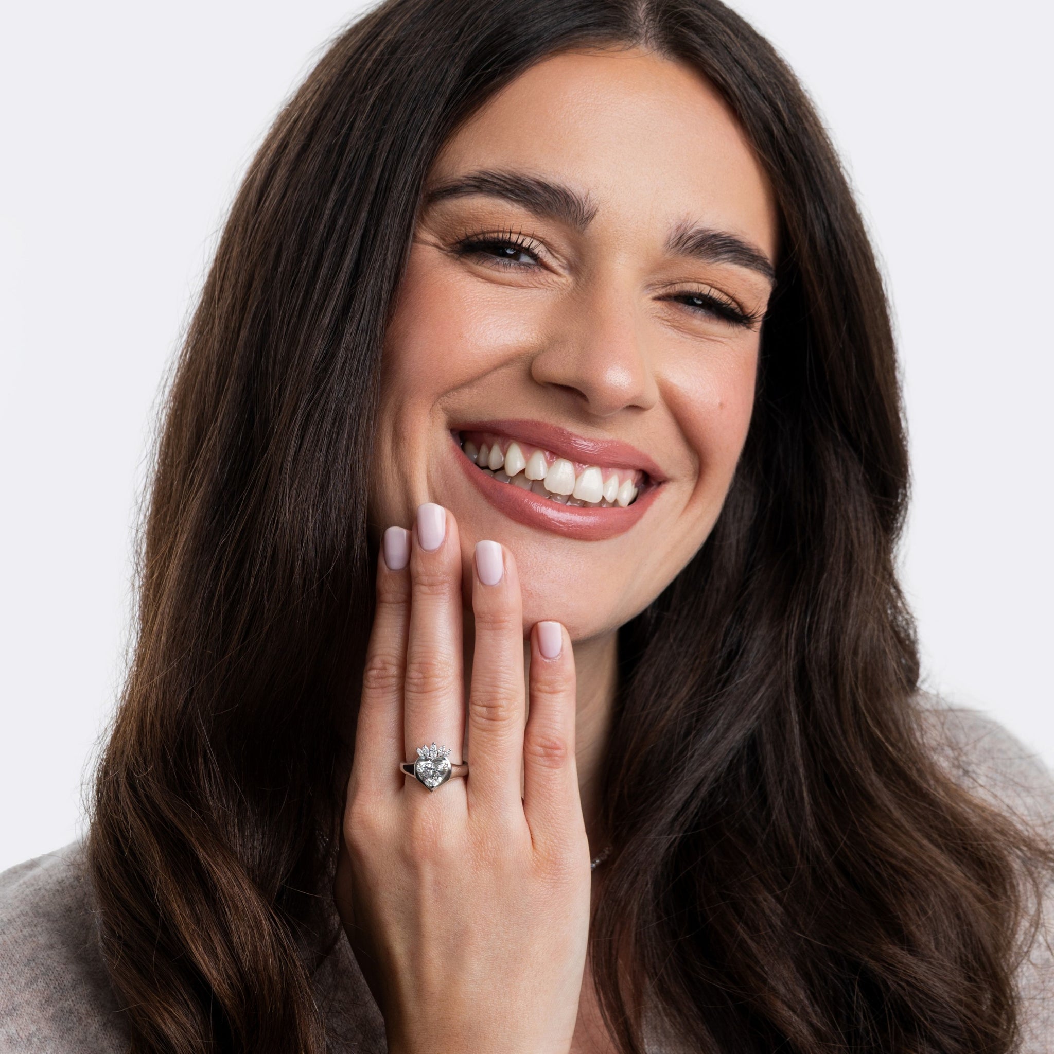 Woman wearing a claddagh ring with a diamond on a plain background