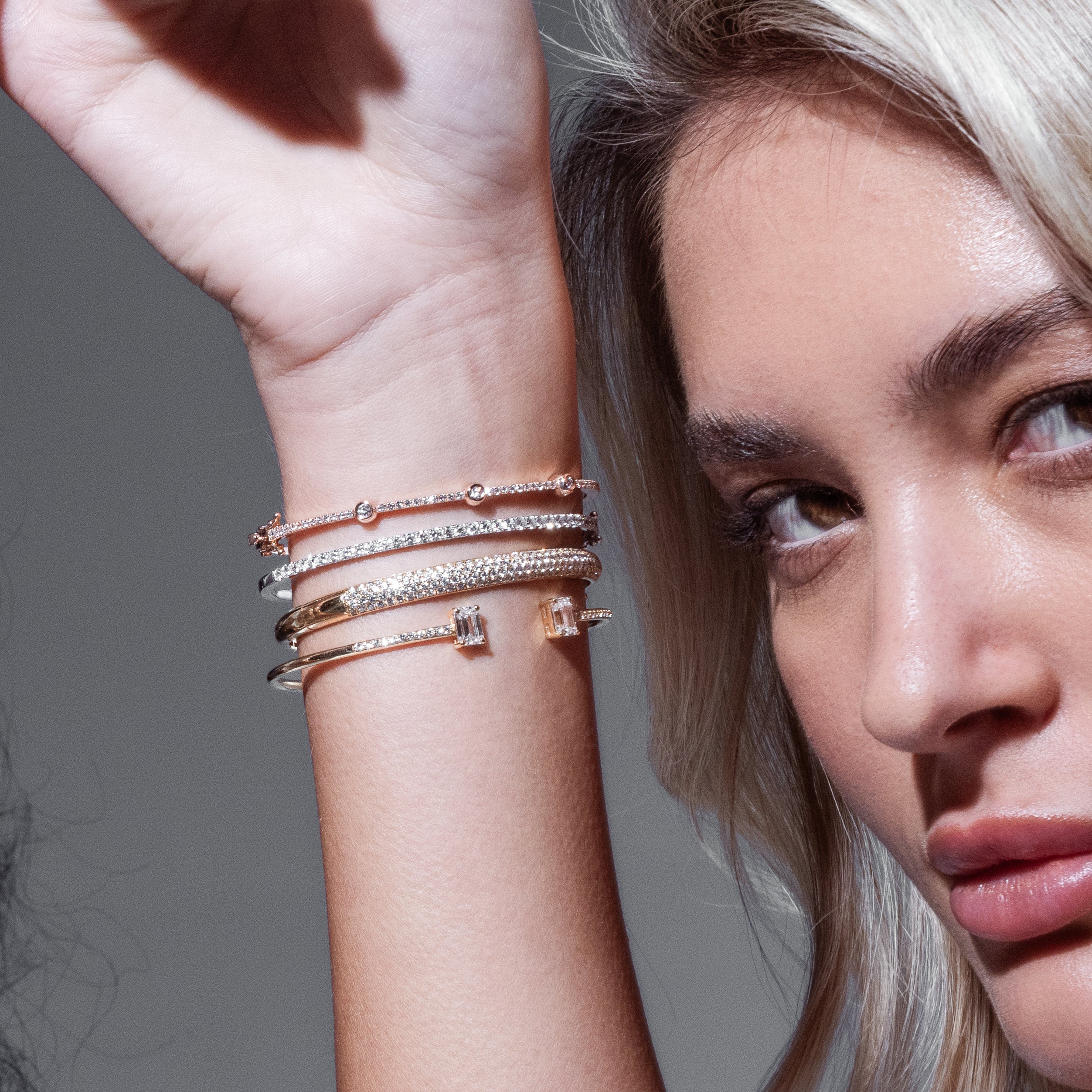 Close-up of a woman's arm wearing multiple diamond bracelets with a neutral background