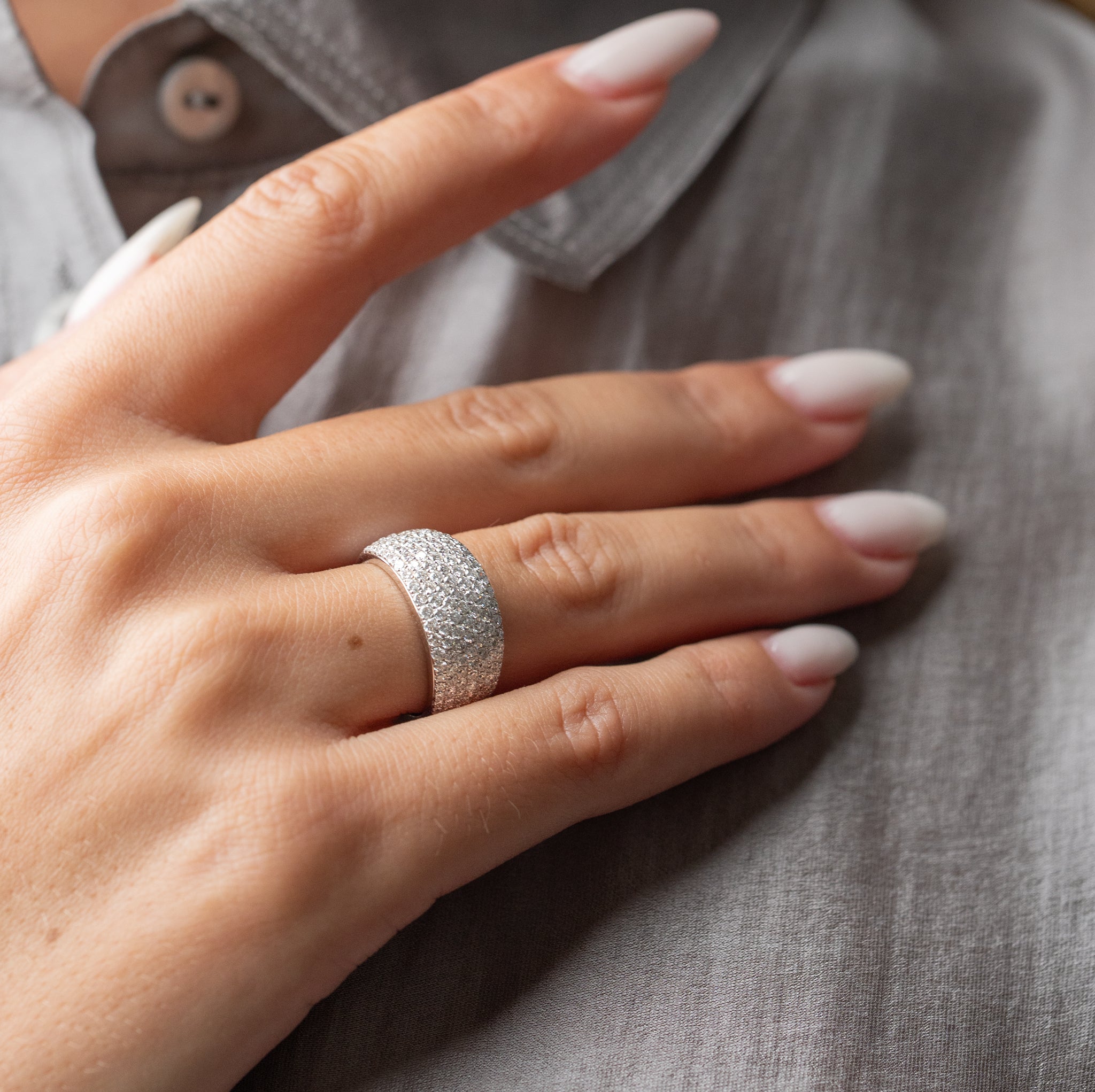 Hand wearing a white gold ring with diamonds against gray fabric background