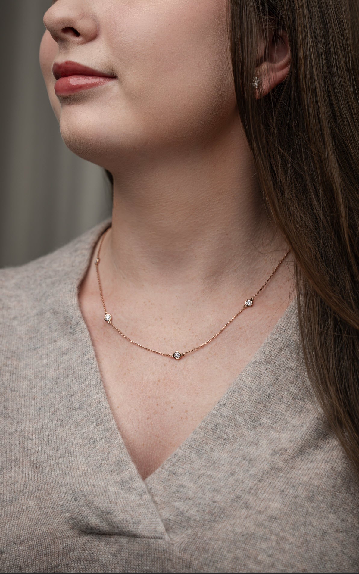 Close-up of a woman wearing a certified diamond necklace on a delicate chain with a beige top.