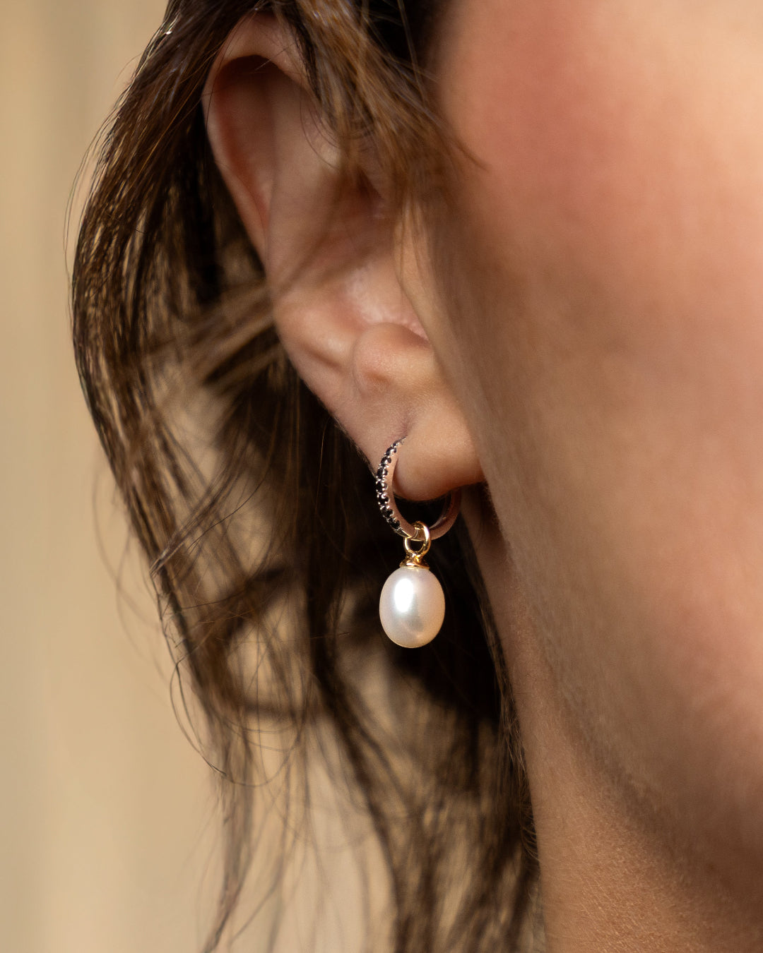 Close-up of a woman's ear wearing pearl earrings with a sleek black diamond hoop.