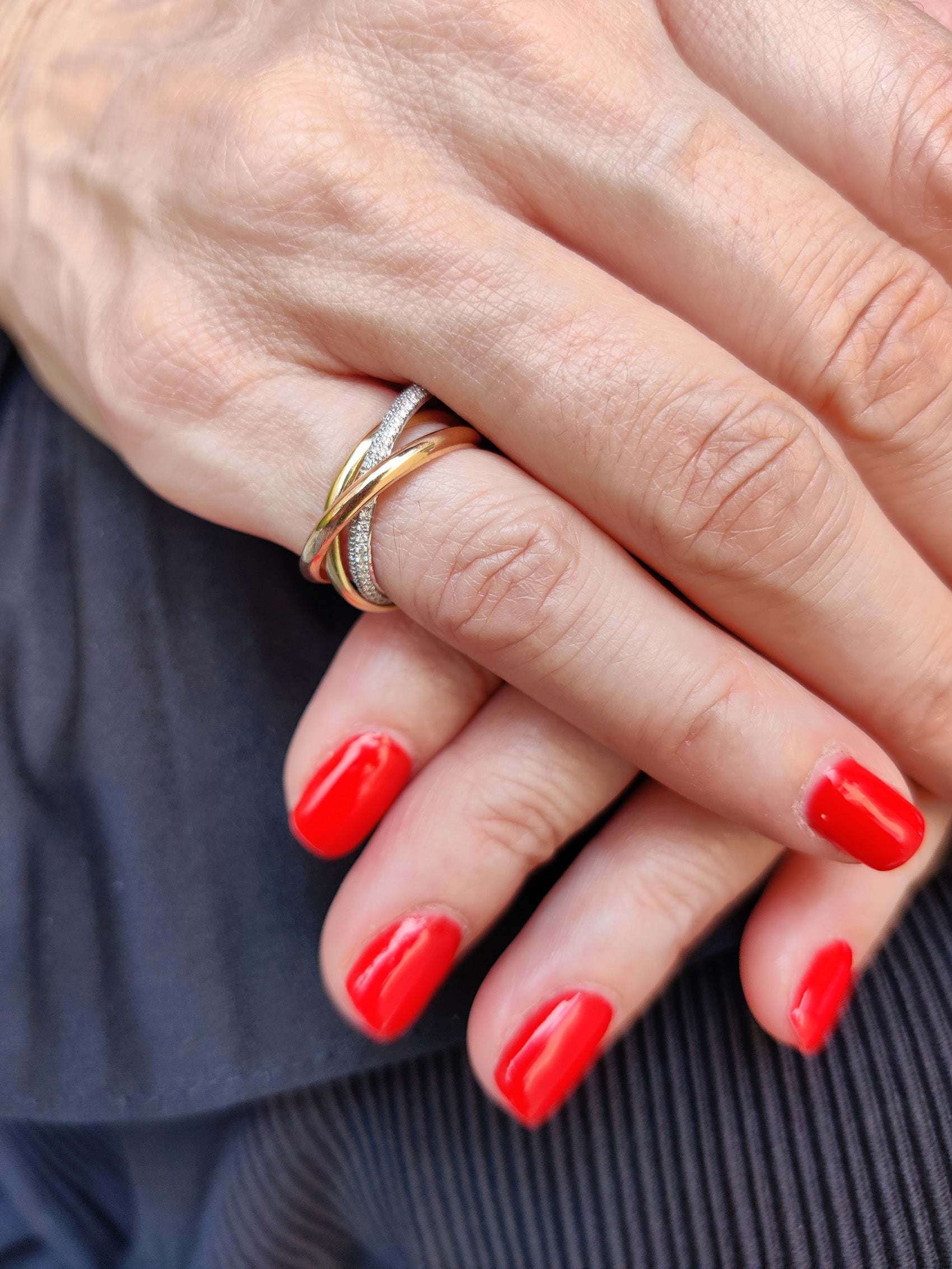 Grace Ring featuring three intertwined solid gold bands and diamonds, elegantly displayed on a hand with red nails.