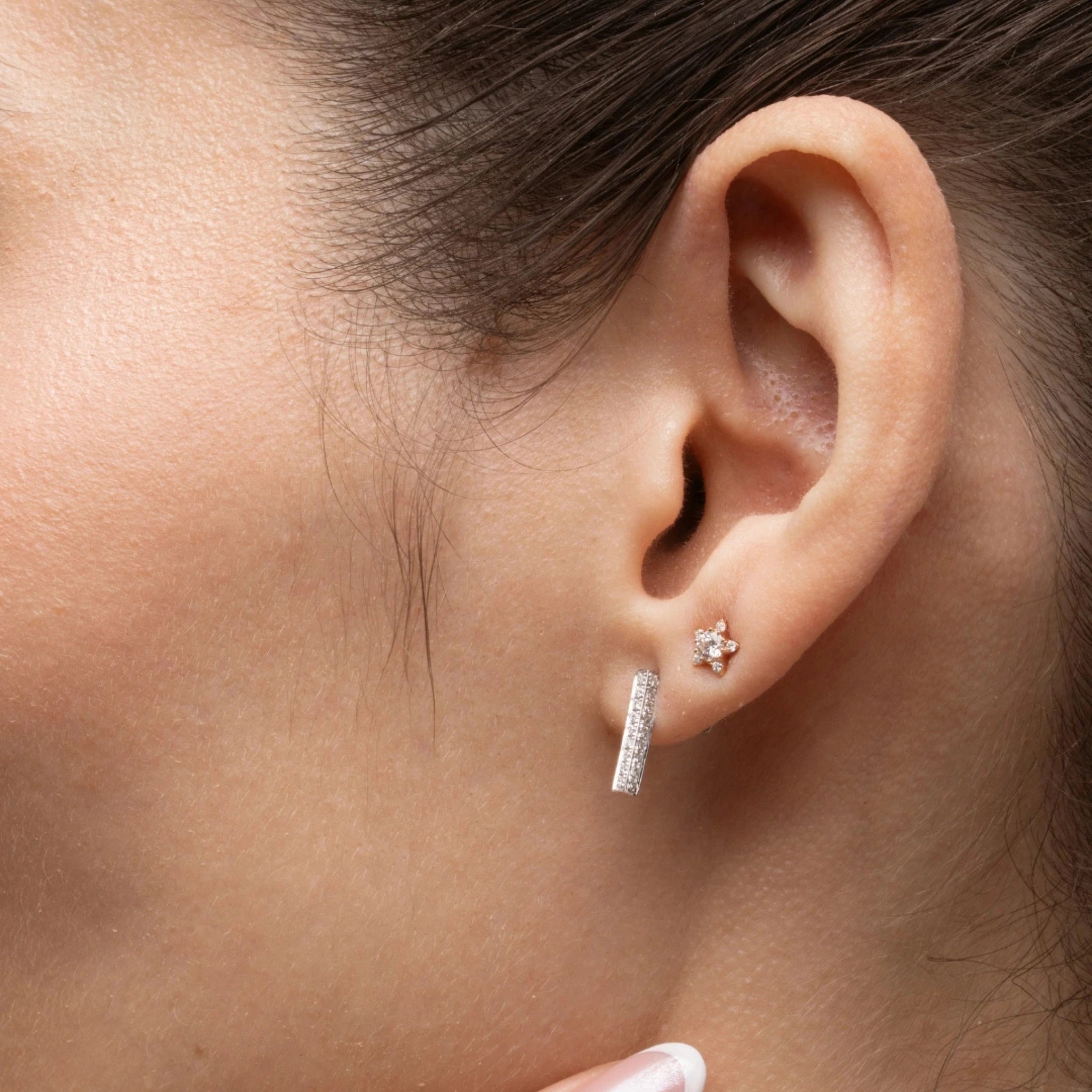 Close-up of a woman's ear adorned with small star earrings featuring certified diamond accents.