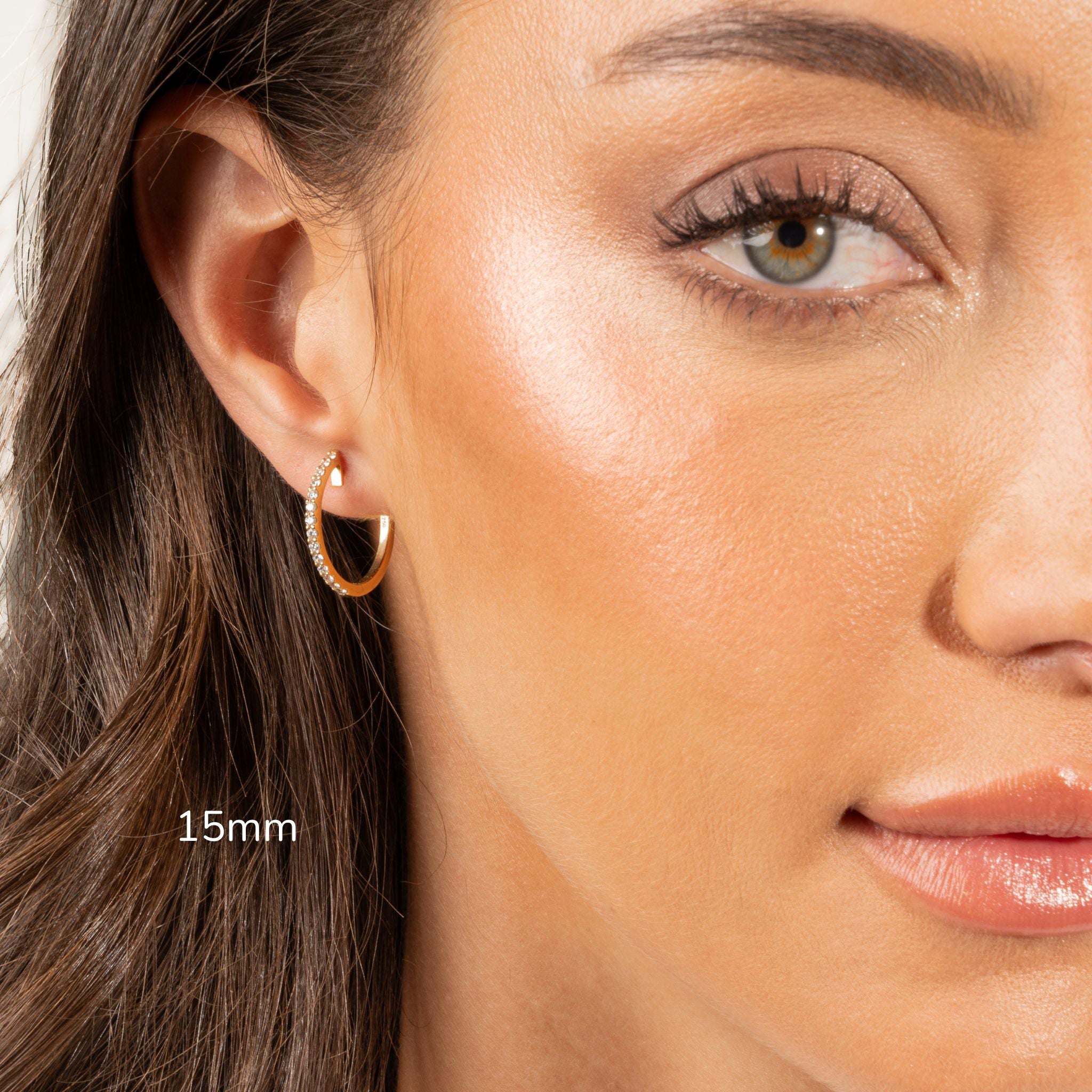 Close-up of a woman wearing diamond hoop earrings with certified diamonds in a gold setting.