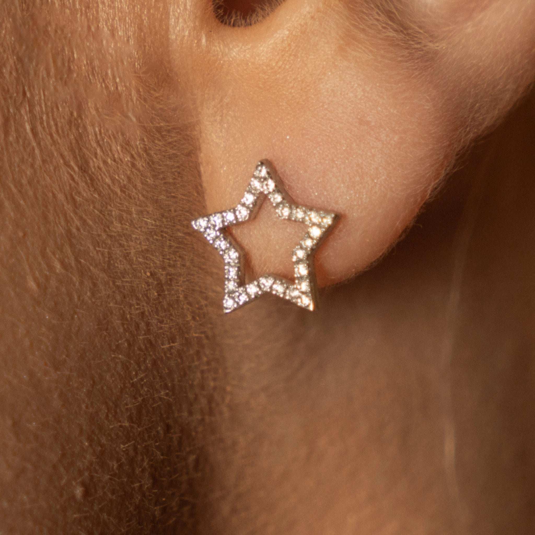 Close up of certified diamond earrings shaped like stars, set in 18ct gold, worn on earlobe.