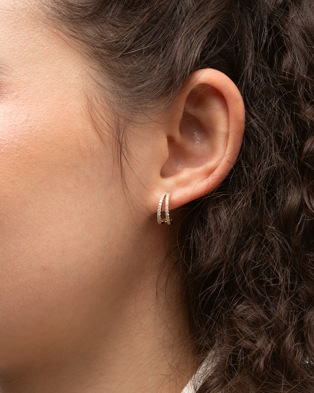 Close up of a model wearing double row diamond huggie earrings made of 18ct gold and certificated diamonds.