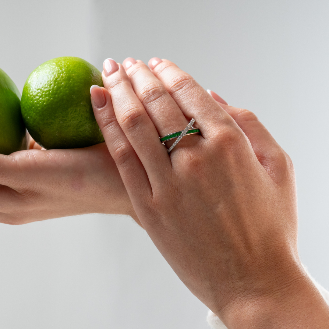 Model wearing an emerald criss cross ring, showcasing its beauty alongside fresh limes in natural setting.