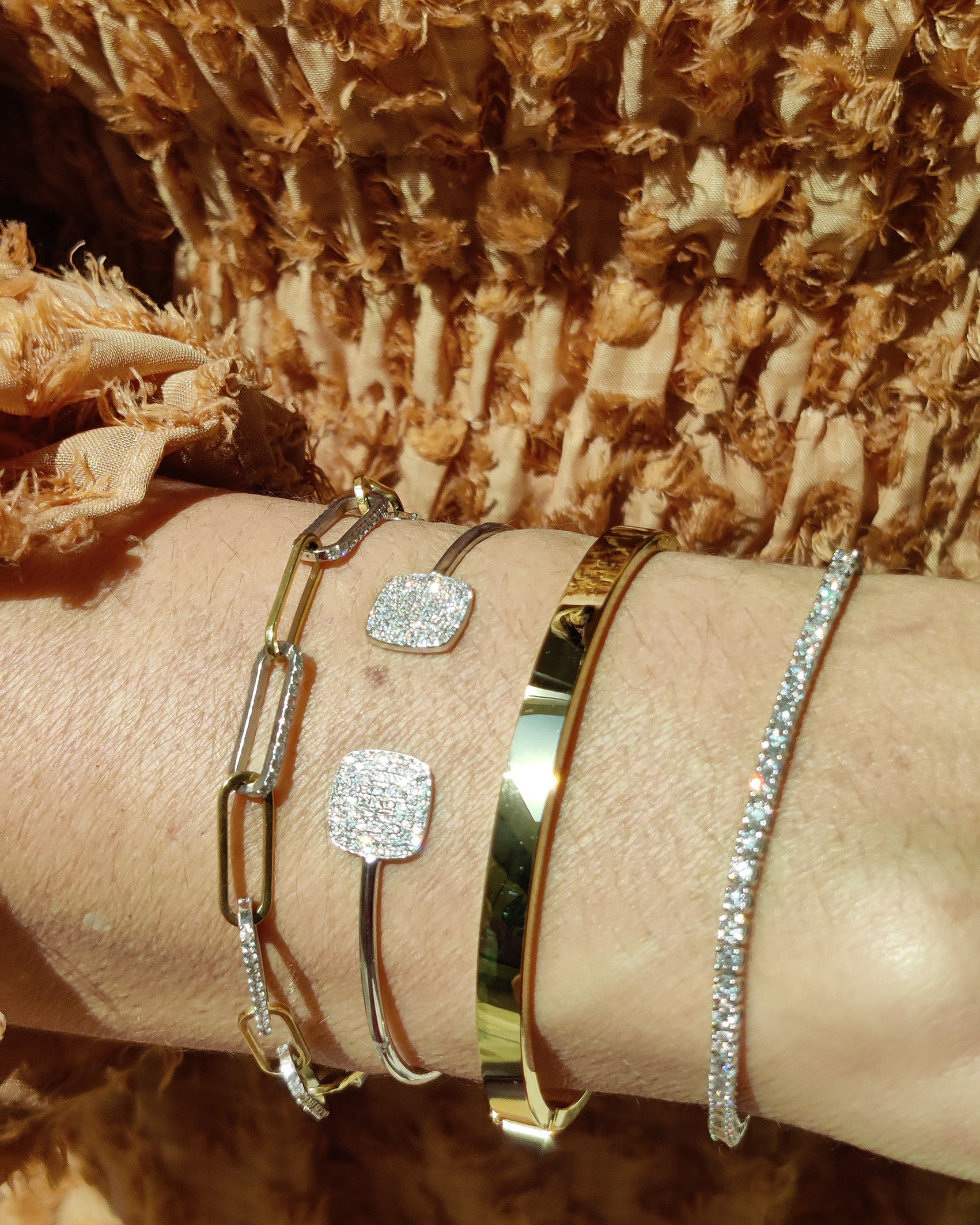 Stylish arm adorned with chain link bracelets featuring diamonds and gold accents.