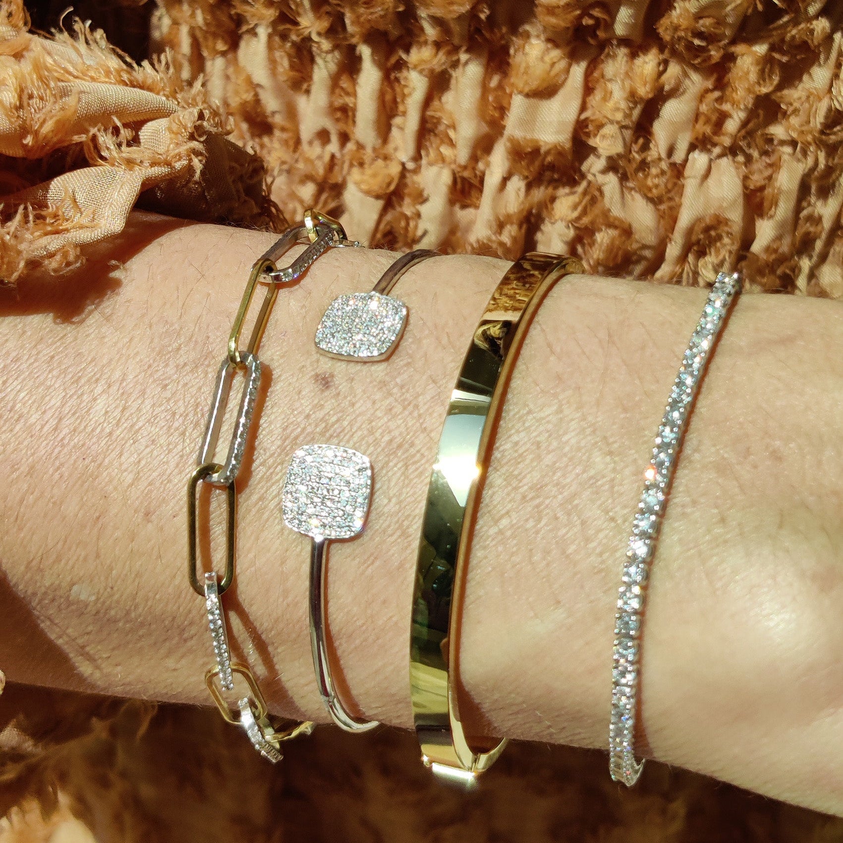 Stylish arm adorned with chain link bracelets featuring diamonds and gold accents.