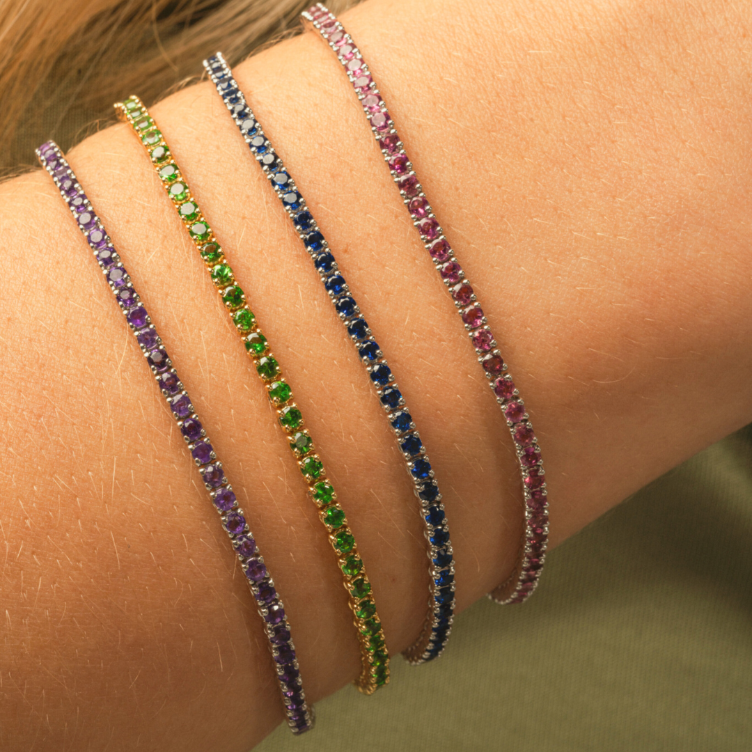 Close-up of multiple colourful gemstone tennis bracelets on a wrist showcasing vibrant hues and elegant design.