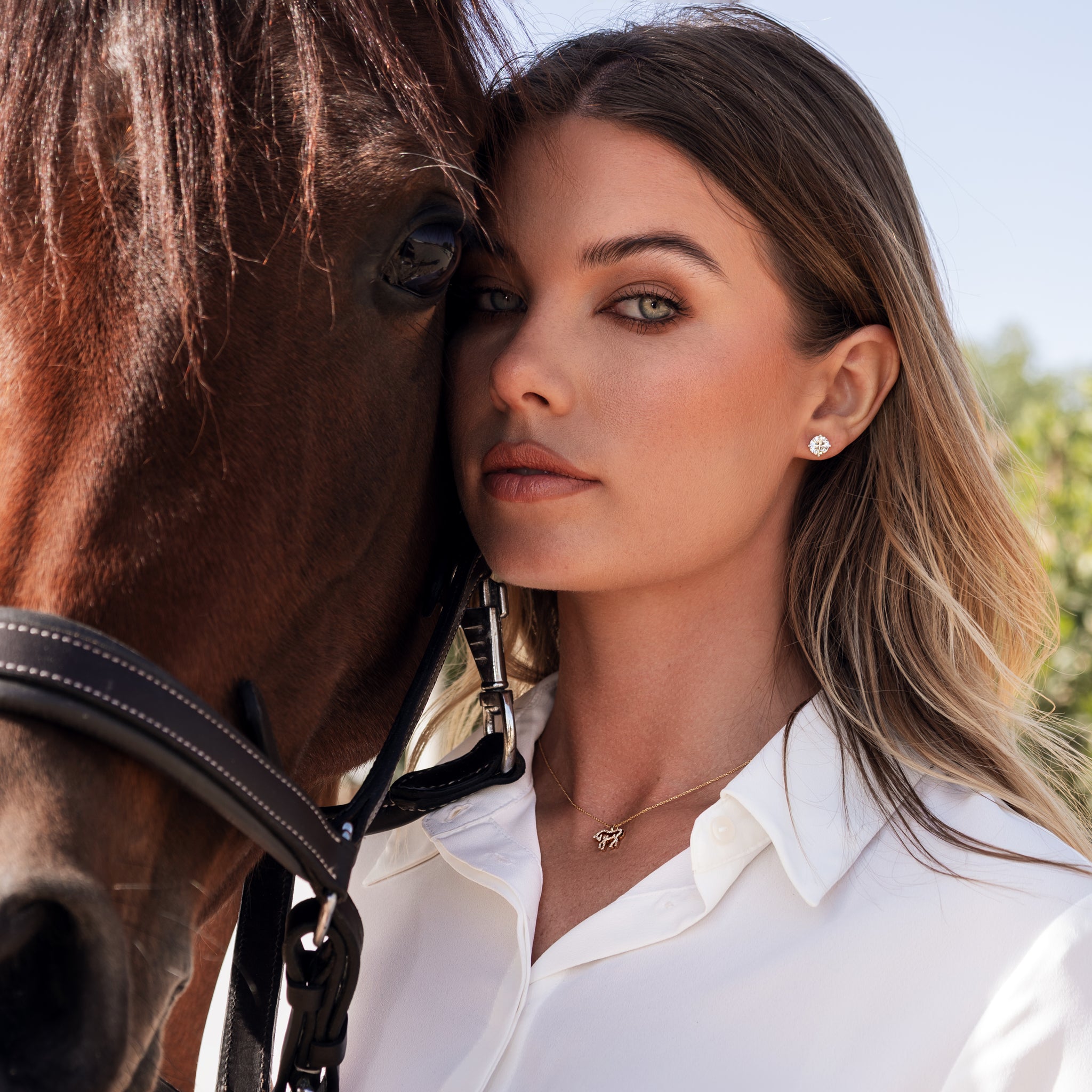 Woman wearing a diamond horse necklace next to a horse with a blurred background