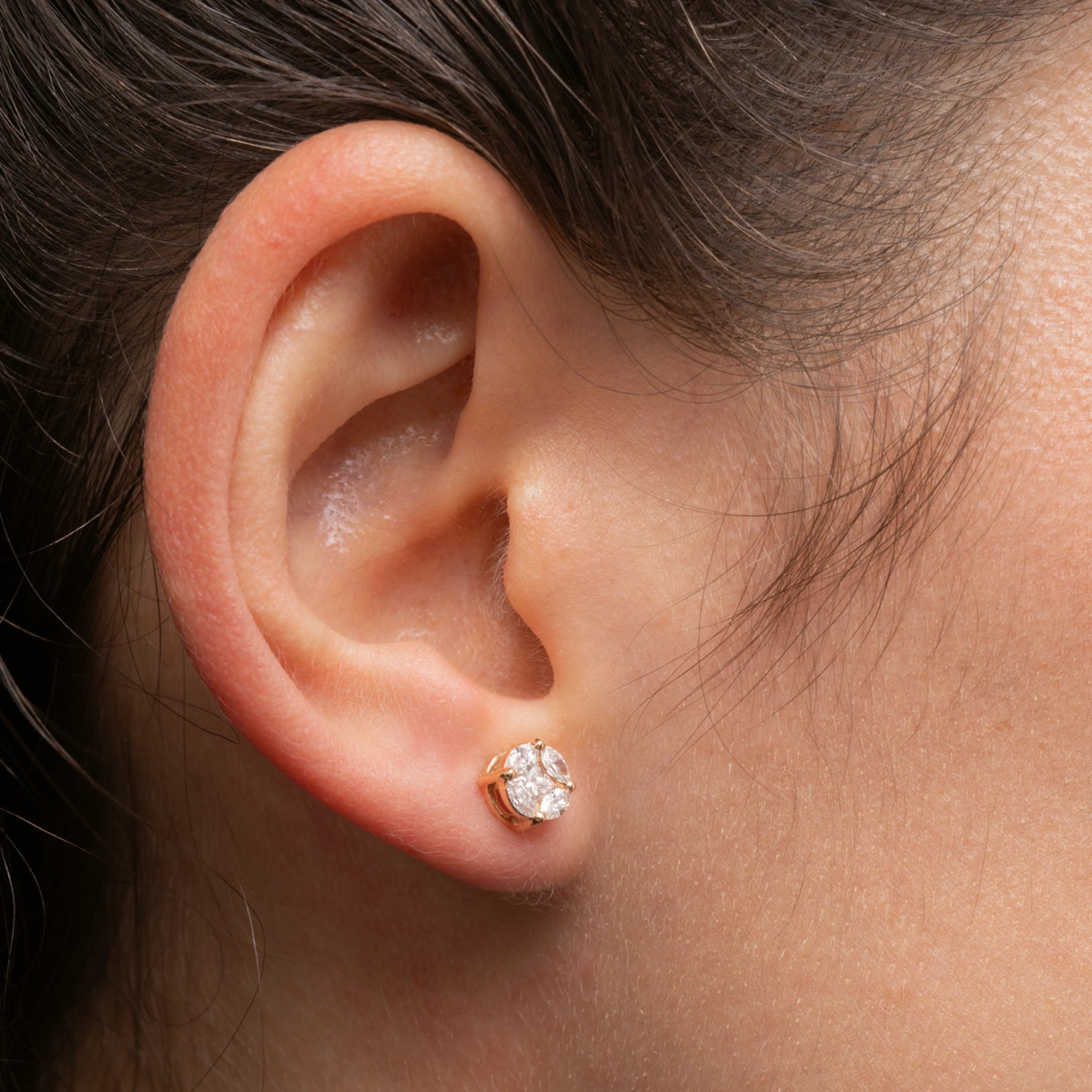 Close-up of an ear wearing a diamond stud earring with a neutral background