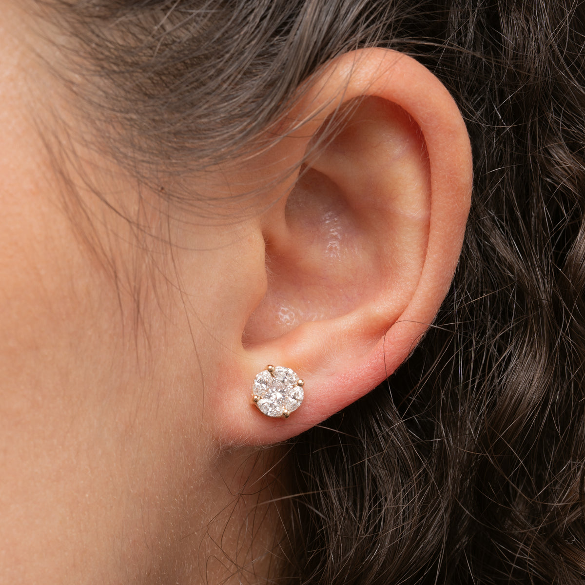 Close-up of an ear wearing a diamond stud earring with hair partially visible.