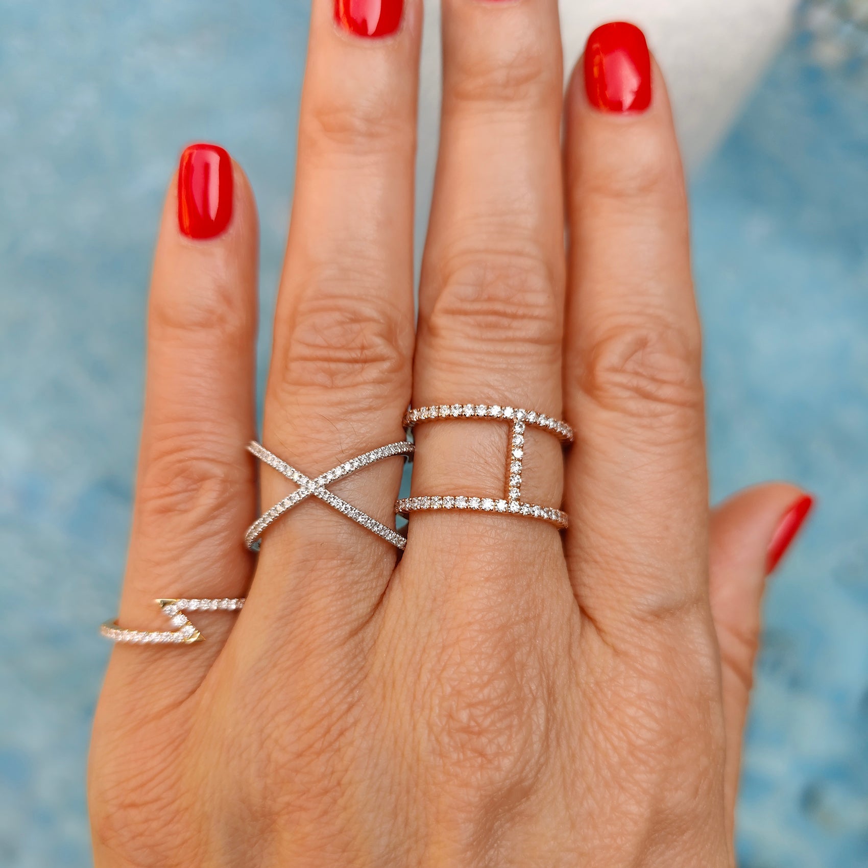 Diamond rings displayed on a hand with red nails, showcasing modern designs and luxurious sparkle.