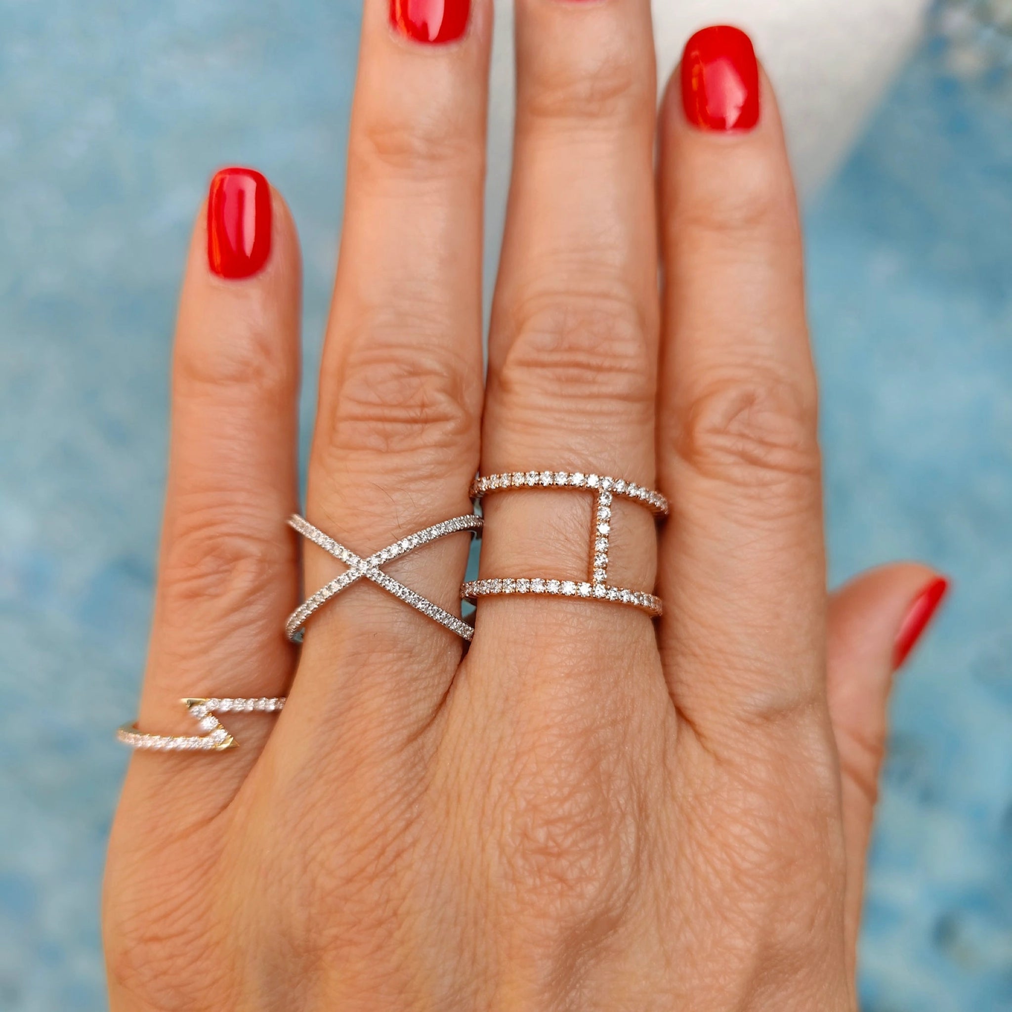 Diamond rings displayed on a hand with red nails, showcasing modern designs and luxurious sparkle.