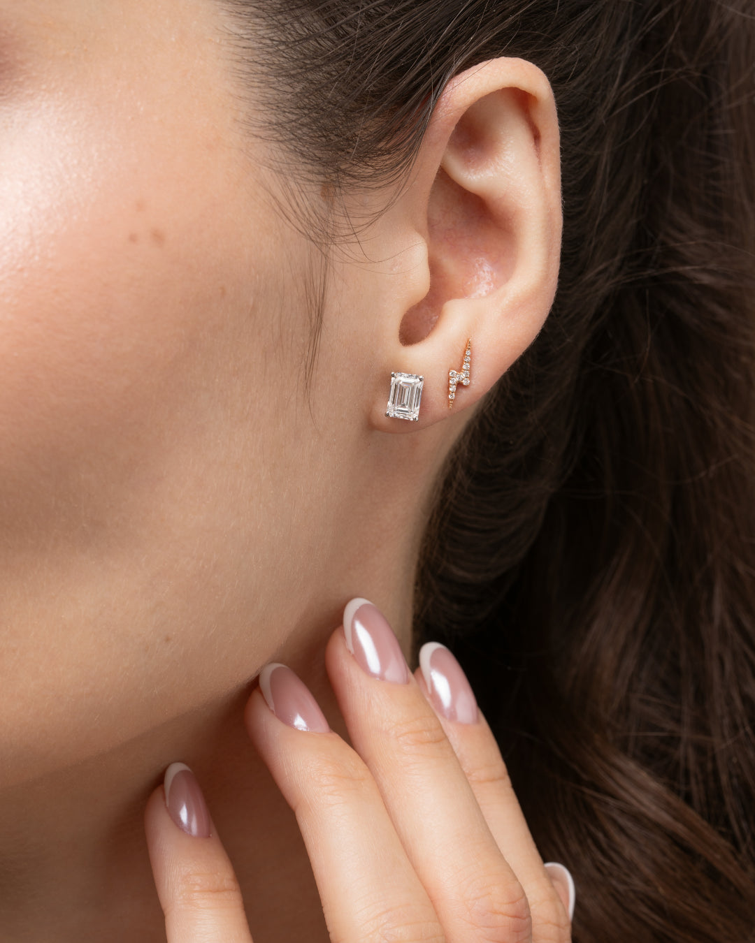 Model showcasing lightning bolt earrings in solid gold with certified diamonds and a stunning emerald cut stud.