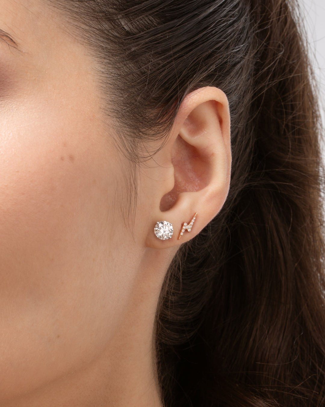 Close-up of a woman's ear showcasing lightning bolt earrings set with certified diamonds, complemented by a sparkling stud earring.