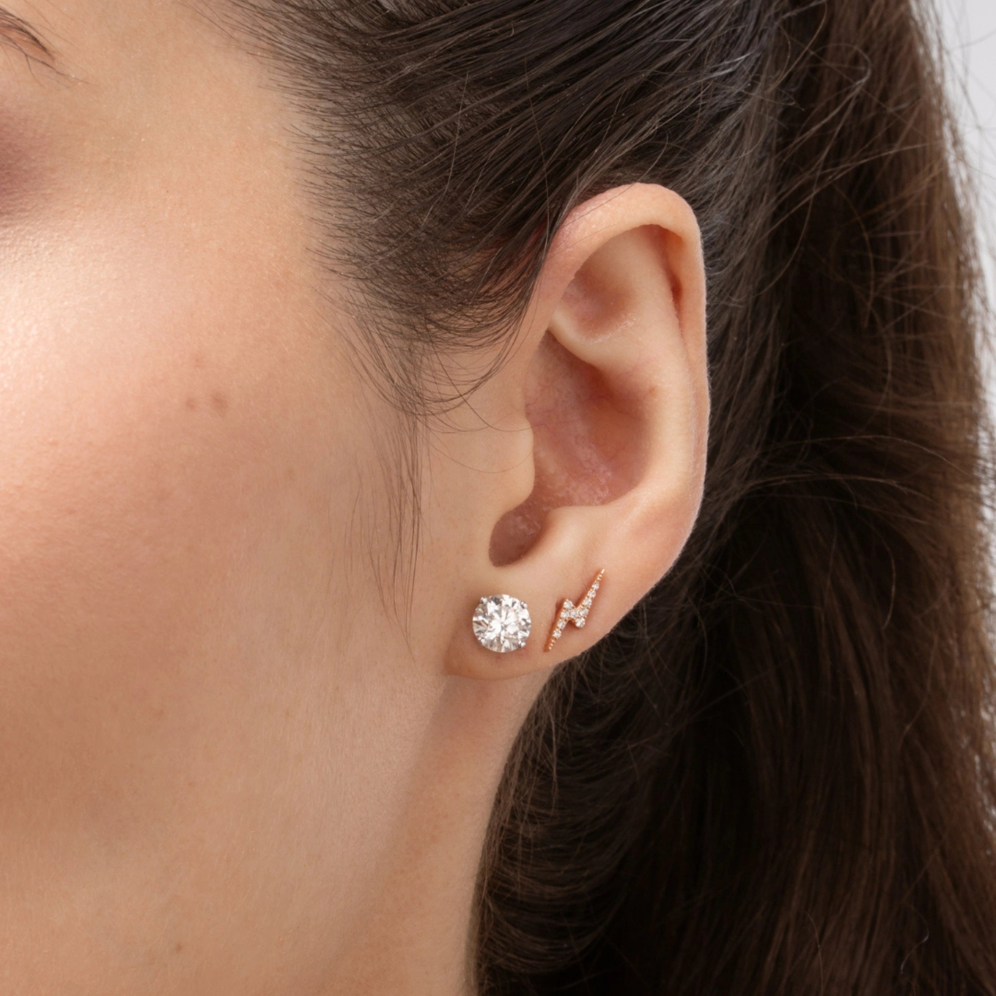 Close-up of a woman's ear showcasing lightning bolt earrings set with certified diamonds, complemented by a sparkling stud earring.