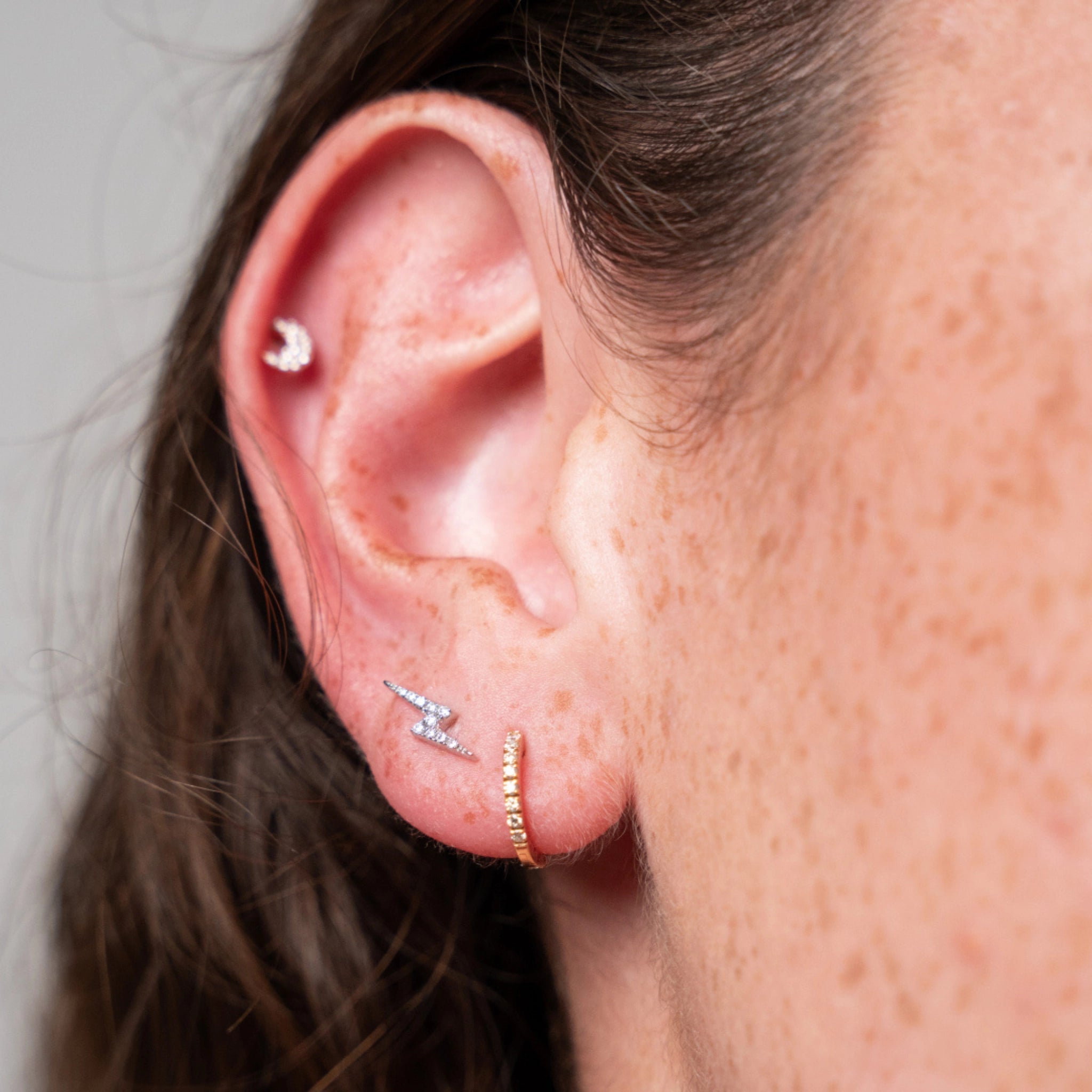 Close-up of ear showcasing lightning bolt earrings set with certified diamonds, highlighting elegance and sparkle.