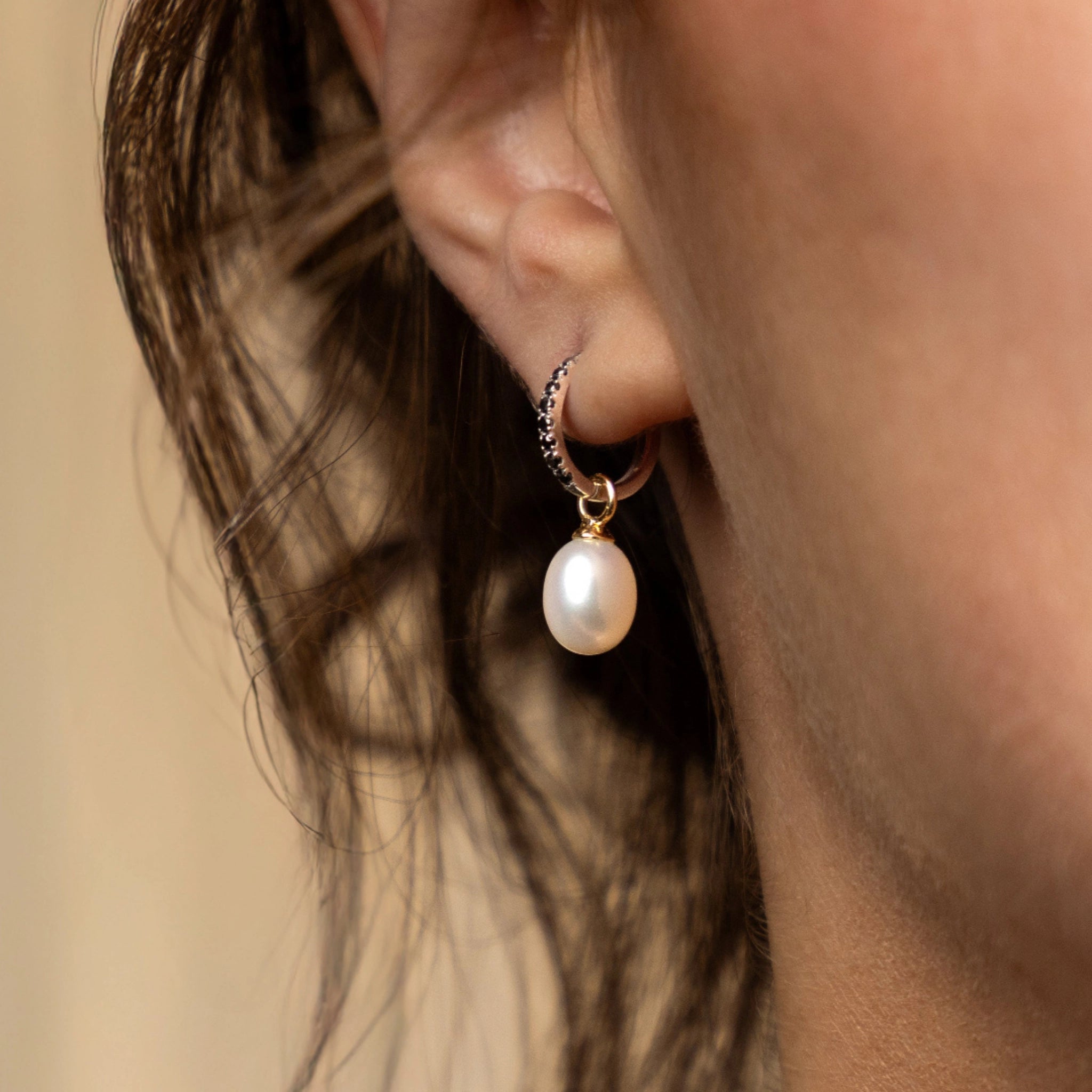 Close-up of a woman's ear wearing pearl earrings with a sleek black diamond hoop.