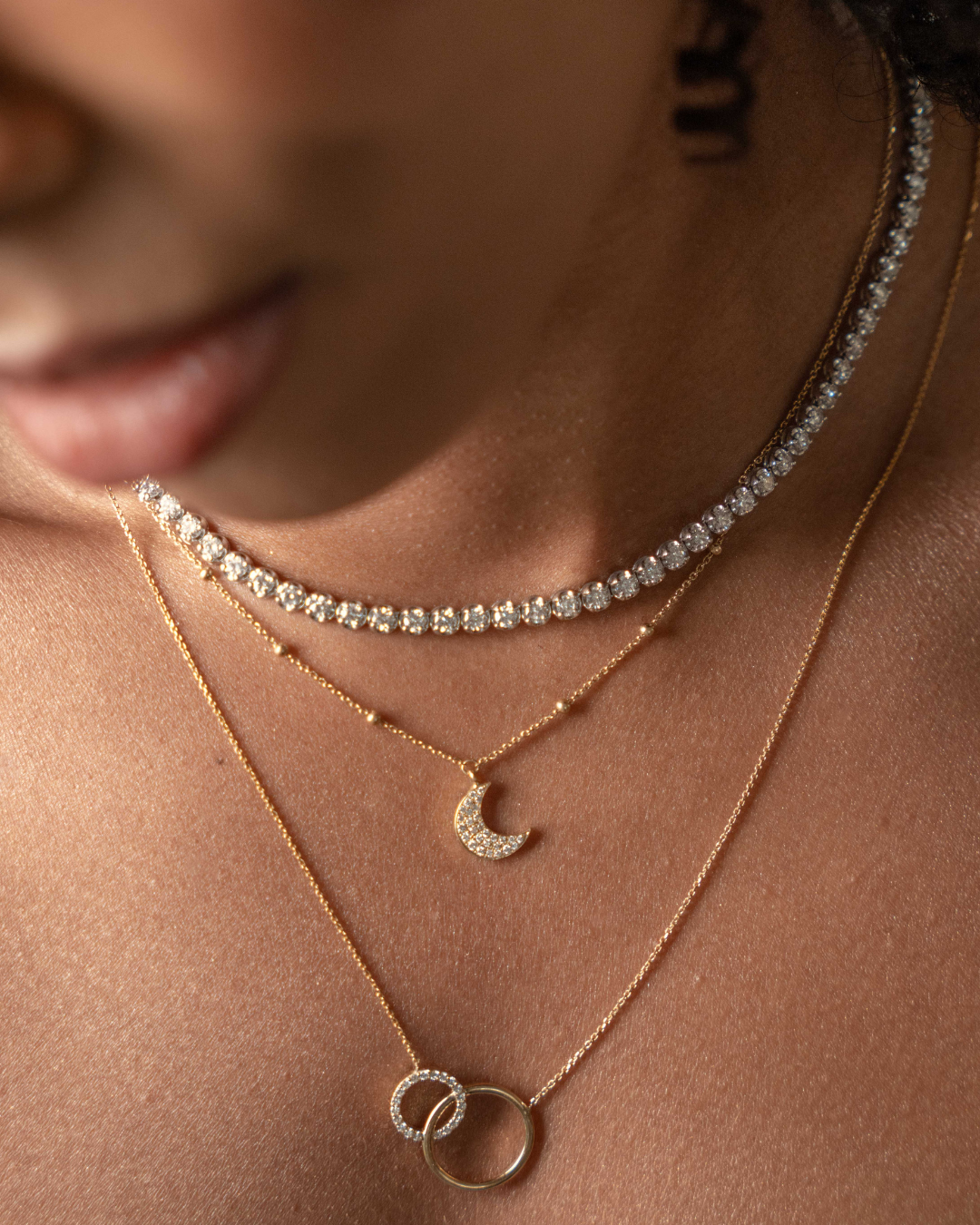 Close-up of layered gold necklaces featuring a diamond necklace with a half moon pendant.