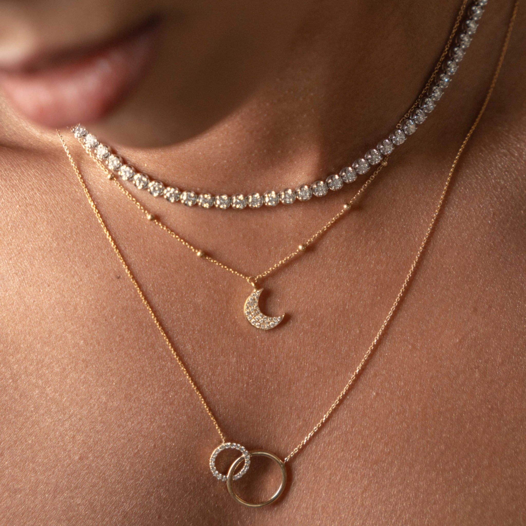 Close-up of layered gold necklaces featuring a diamond necklace with a half moon pendant.