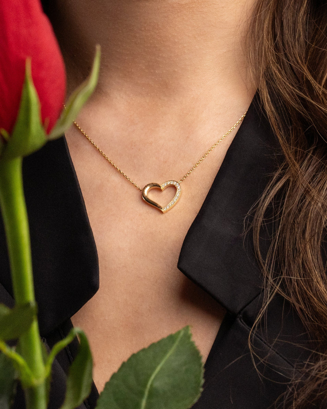 Gold and diamond heart necklace worn by a woman with a red rose in the foreground