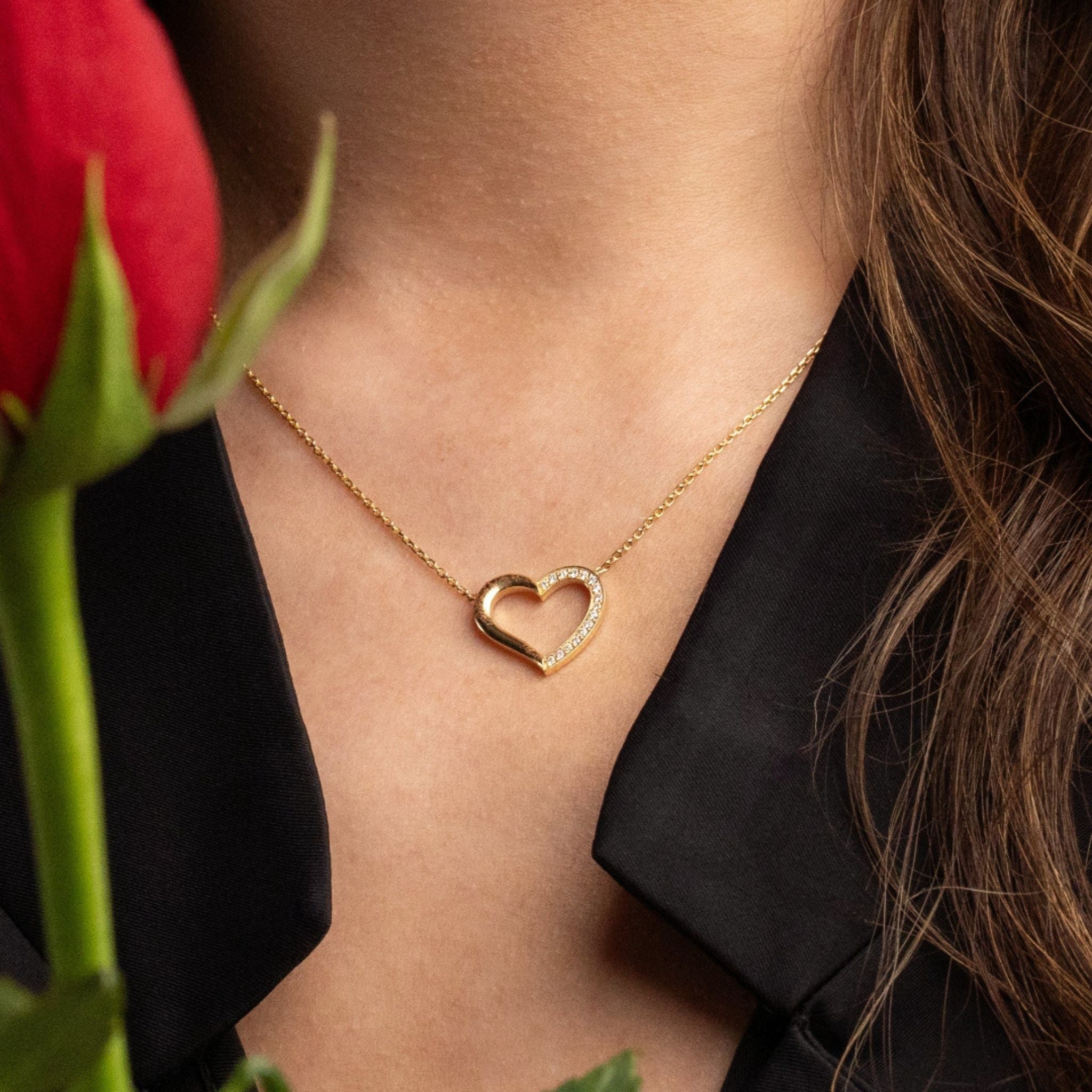 Gold and diamond heart necklace worn by a woman with a red rose in the foreground