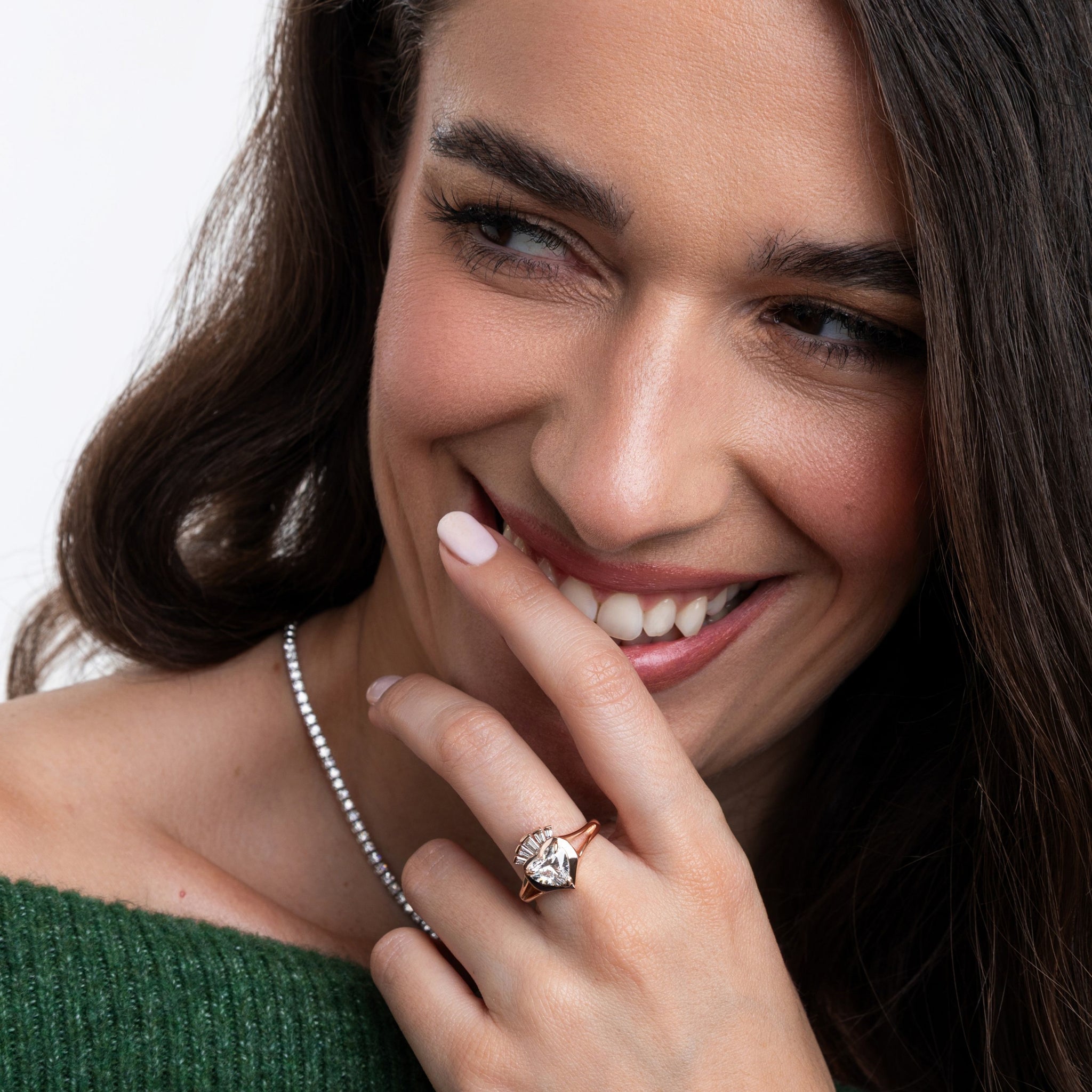 Woman wearing a modern claddagh ring with diamonds and a diamond tennis necklace, smiling.