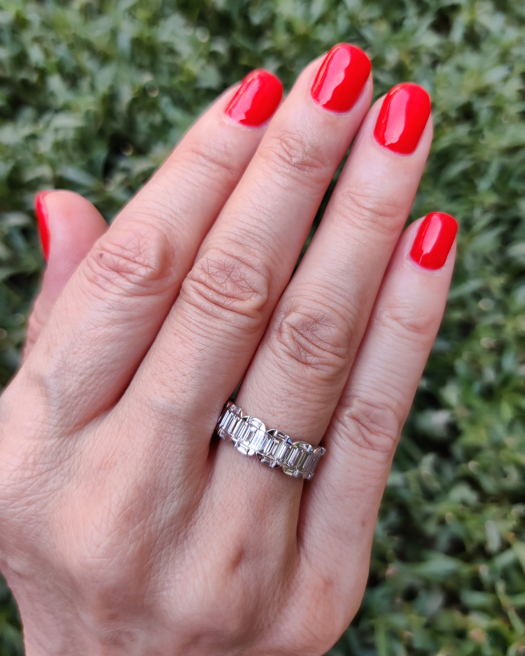 Hand wearing a baguette cluster eternity ring showcasing natural diamonds on a grassy background.