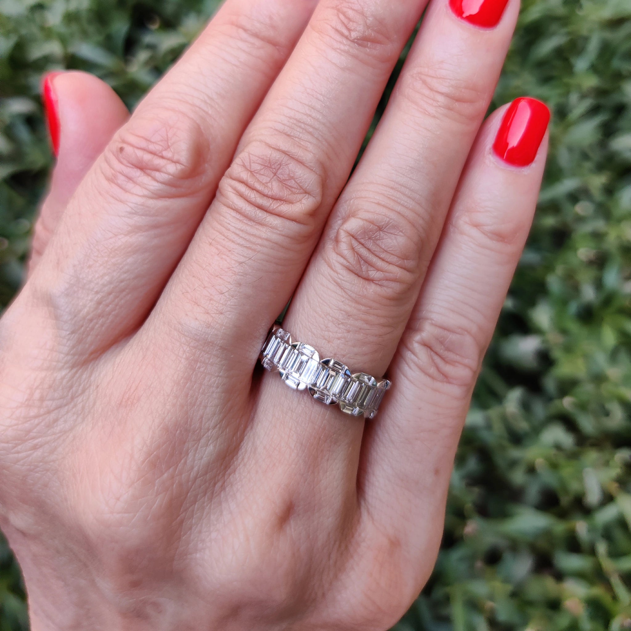 Hand wearing a baguette cluster eternity ring showcasing natural diamonds on a grassy background.