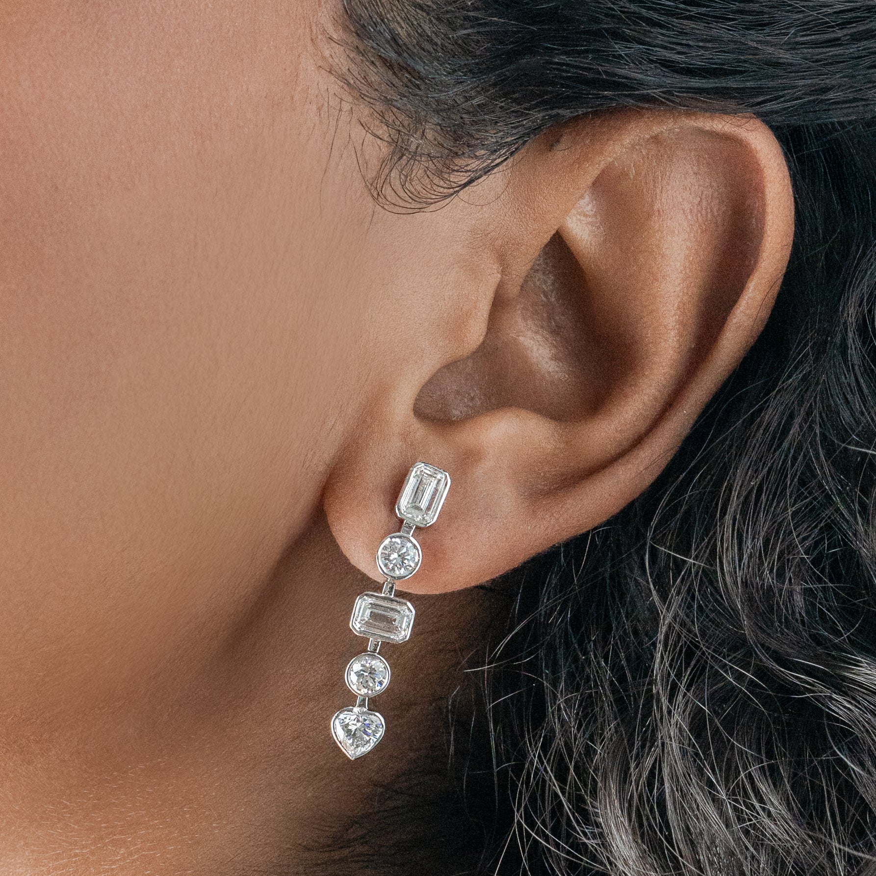 Close-up of an ear wearing a diamond earring with a neutral background