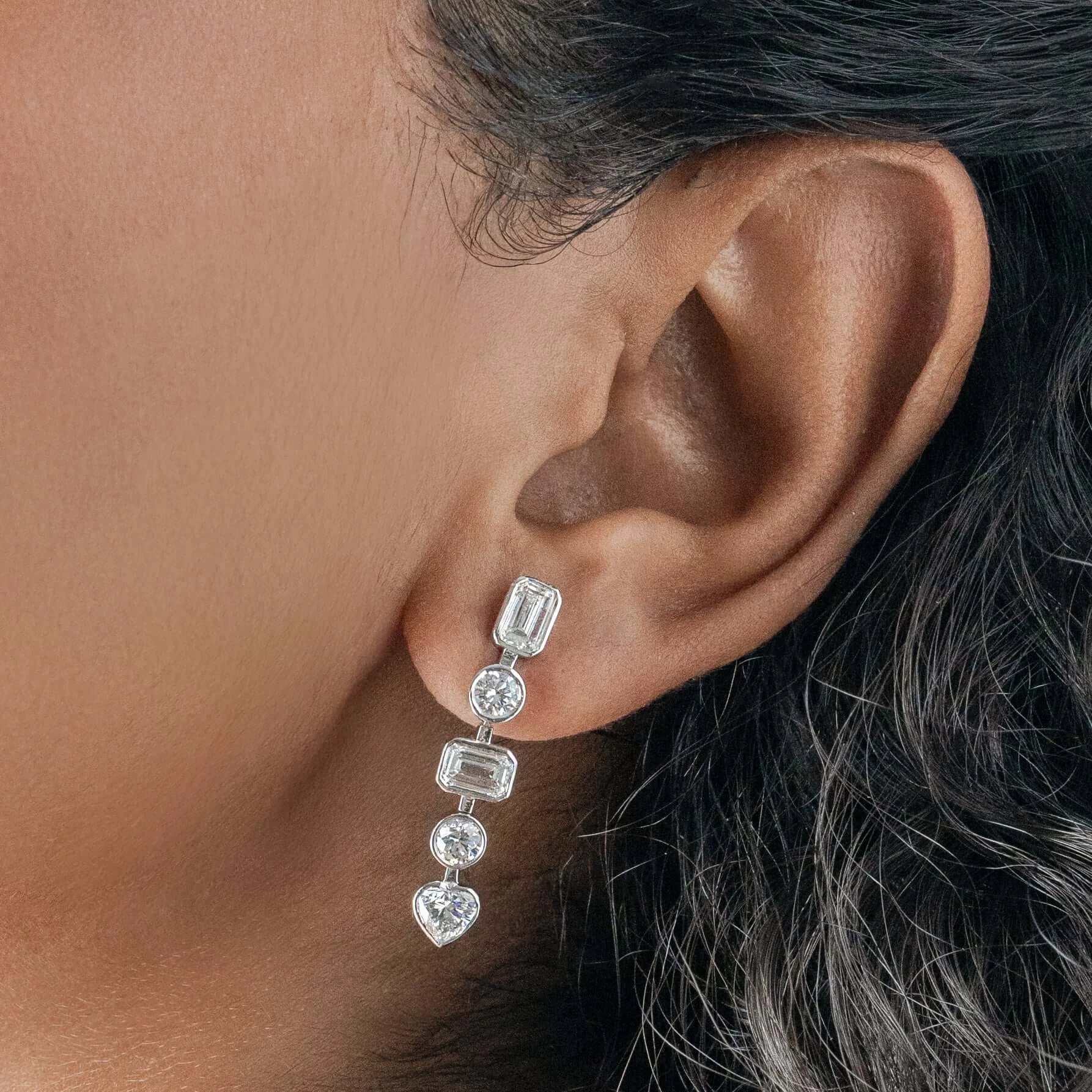 Close-up of an ear wearing a diamond earring with a neutral background