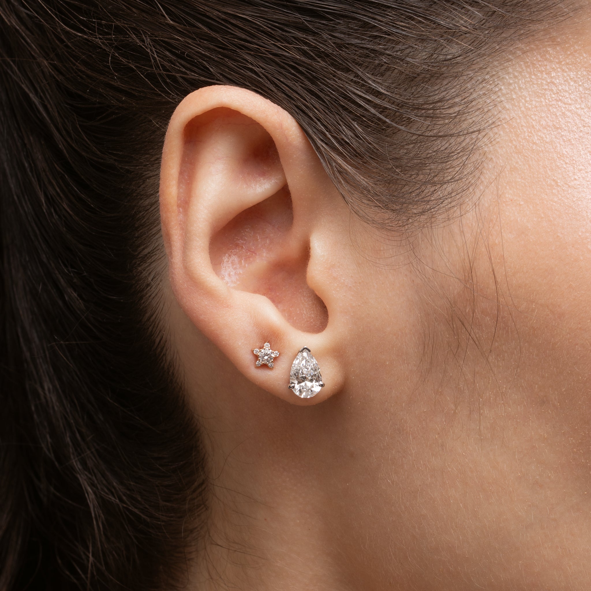 Pear Diamond Stud Earrings showcased in a woman's ear, featuring a sparkling pear shape diamond and a small star earring.