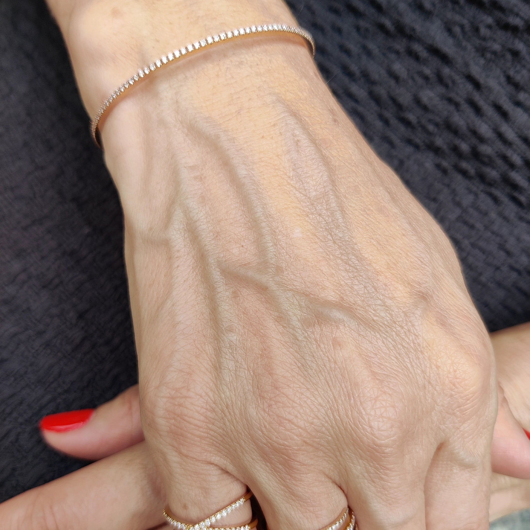 Elegant push-on tennis bangle with diamonds stacked with rings on a hand.