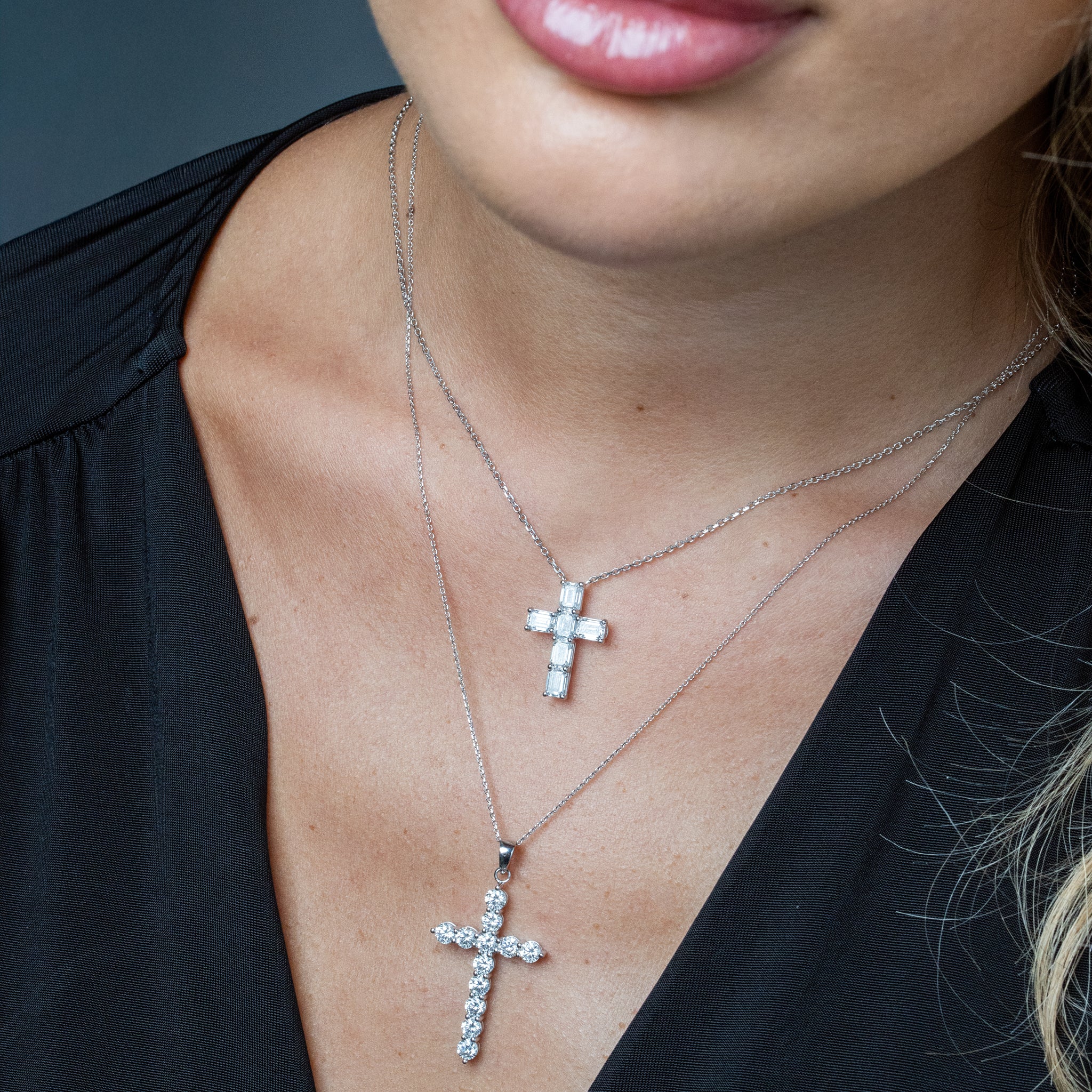 Close-up of a person wearing two diamond cross necklaces with a blurred background