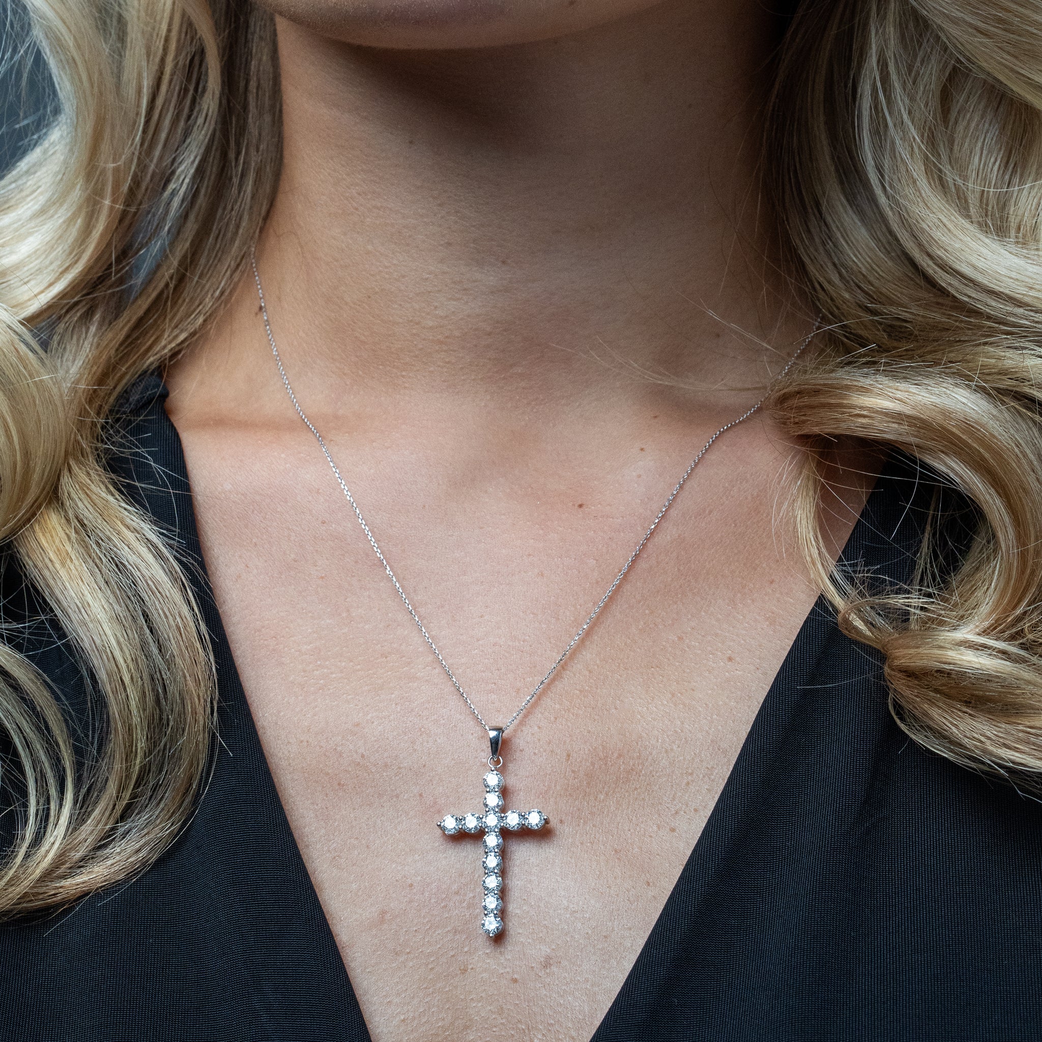 Close-up of a person wearing a white gold diamond cross necklace with a black top.