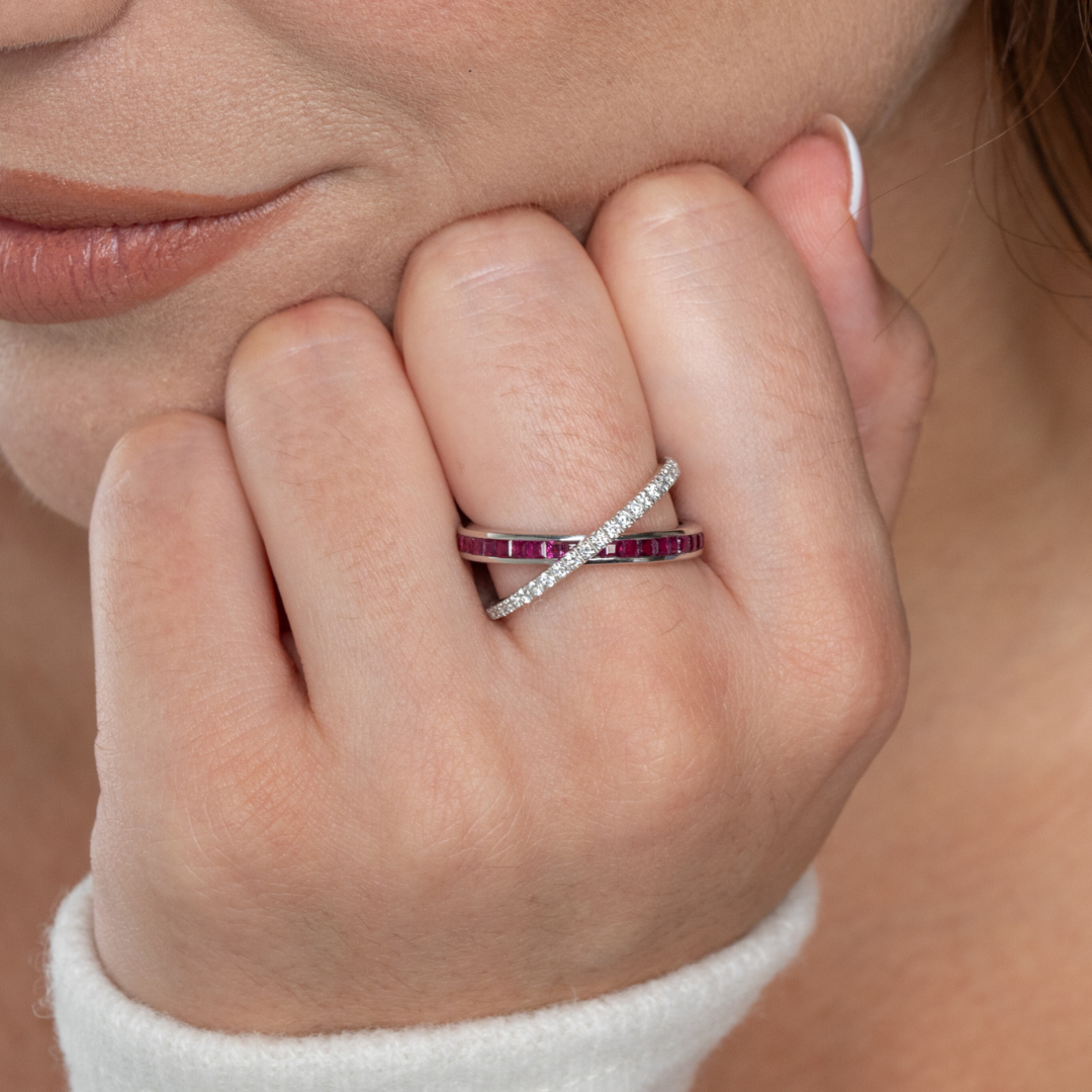 Close-up of a woman's hand wearing a ruby criss cross ring featuring red rubies and diamonds.